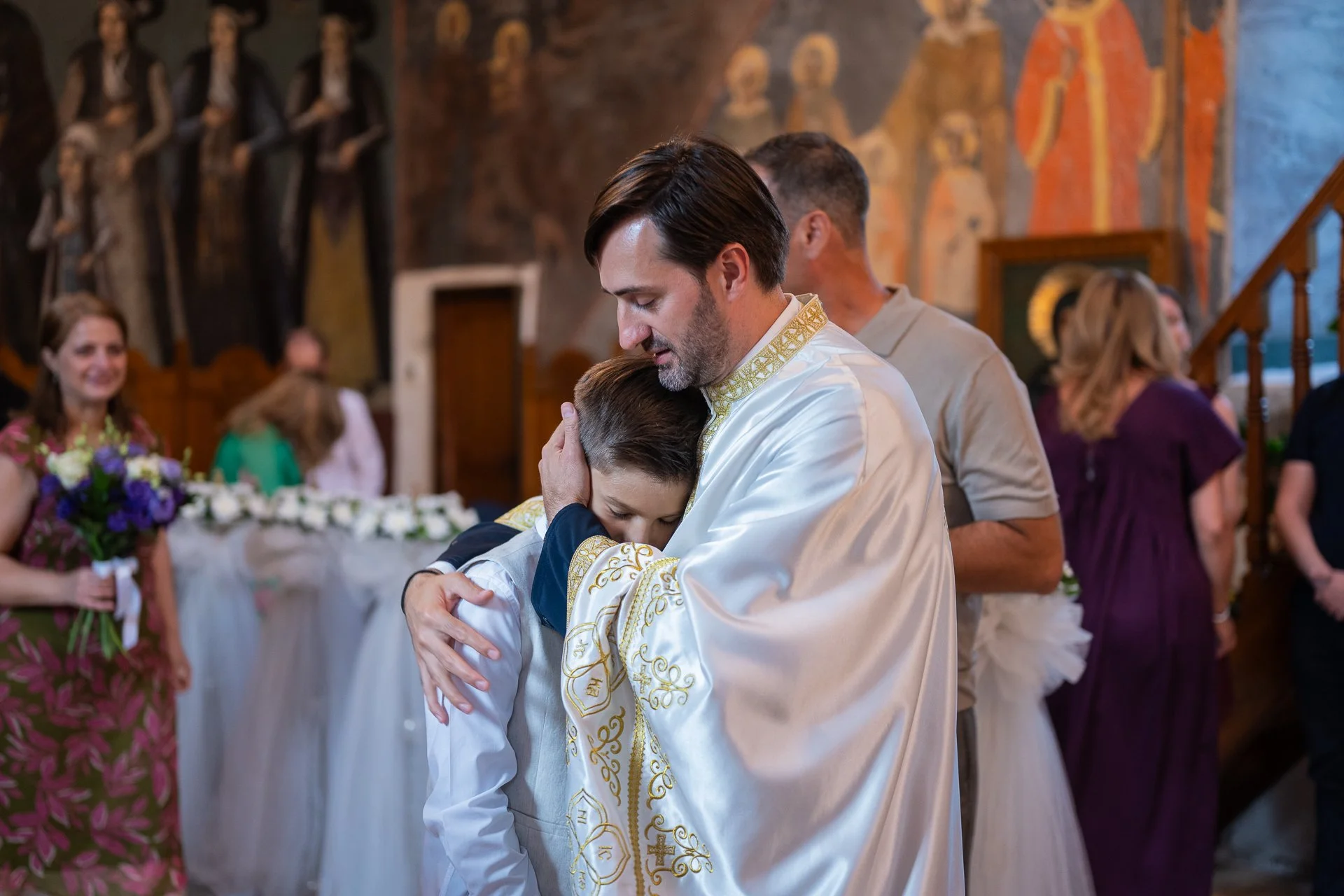 parintele il tine la pieptul lui pe un baietel care este fratele mai mare al bebelusului botezat