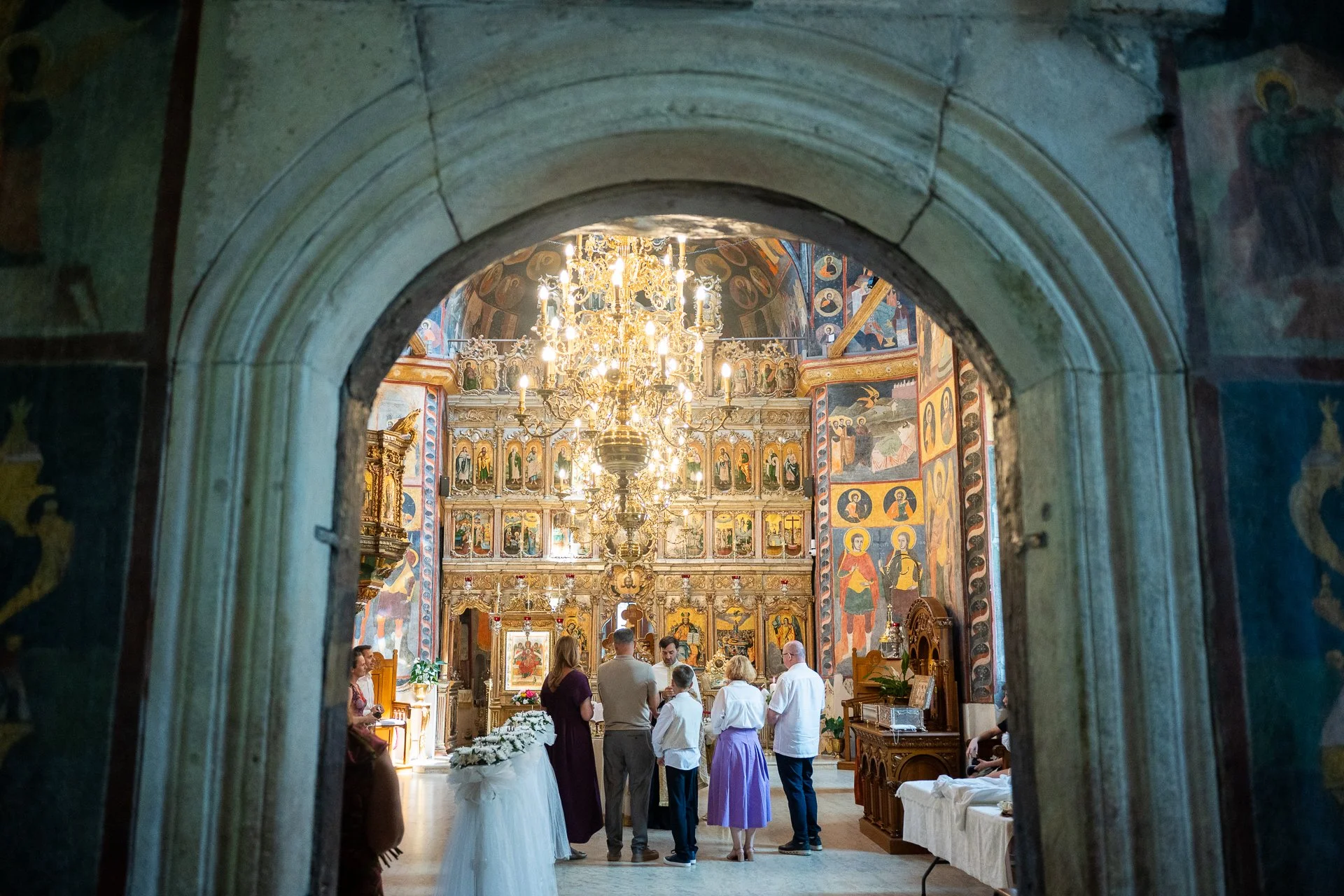 grupul de nasi si parinti la botez sunt fotografiati din spate printr o arcada 