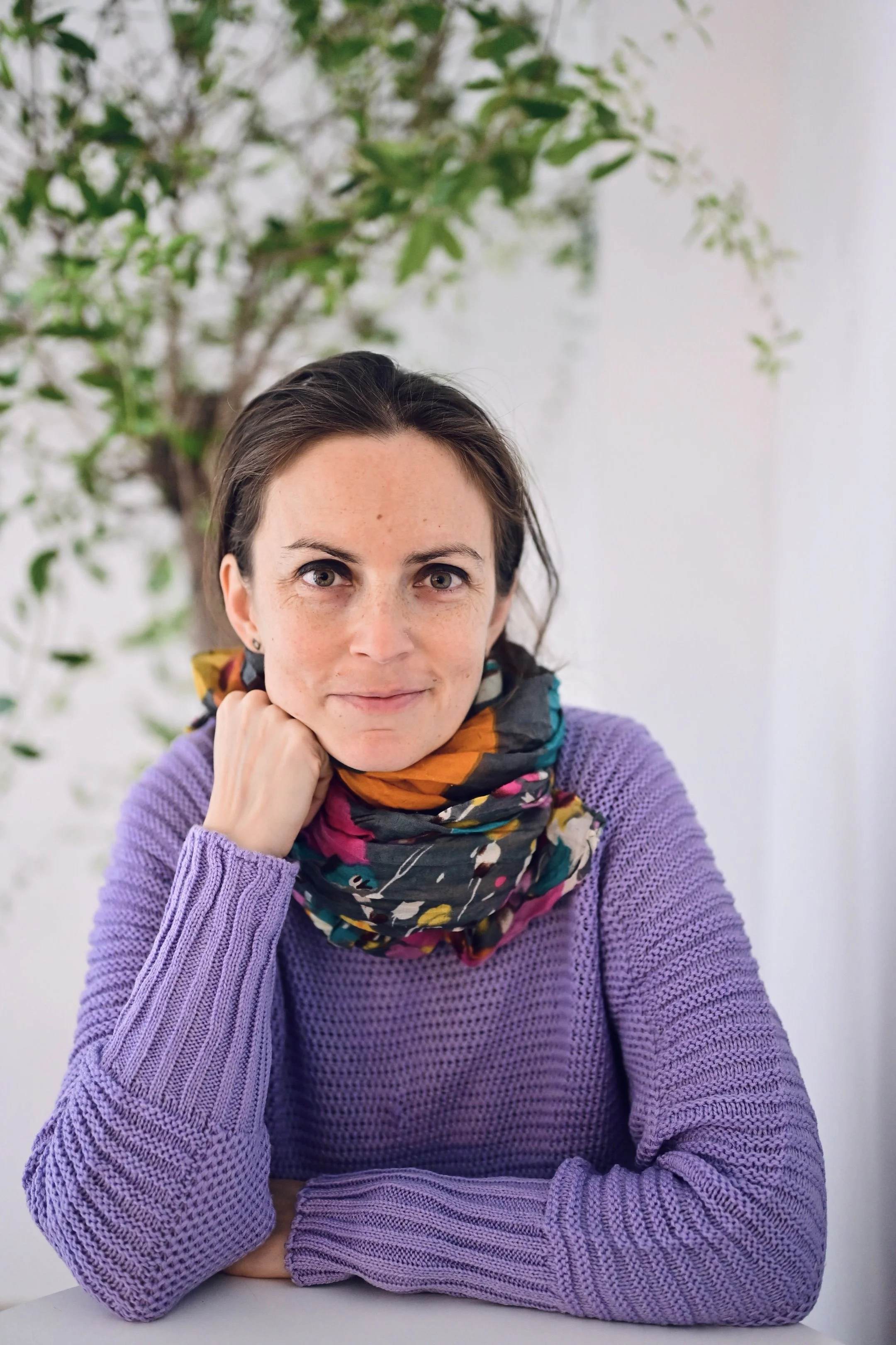 o tanara care sta sprijinita cu coatele pe o masa gri si care zambeste spre aparatul foto