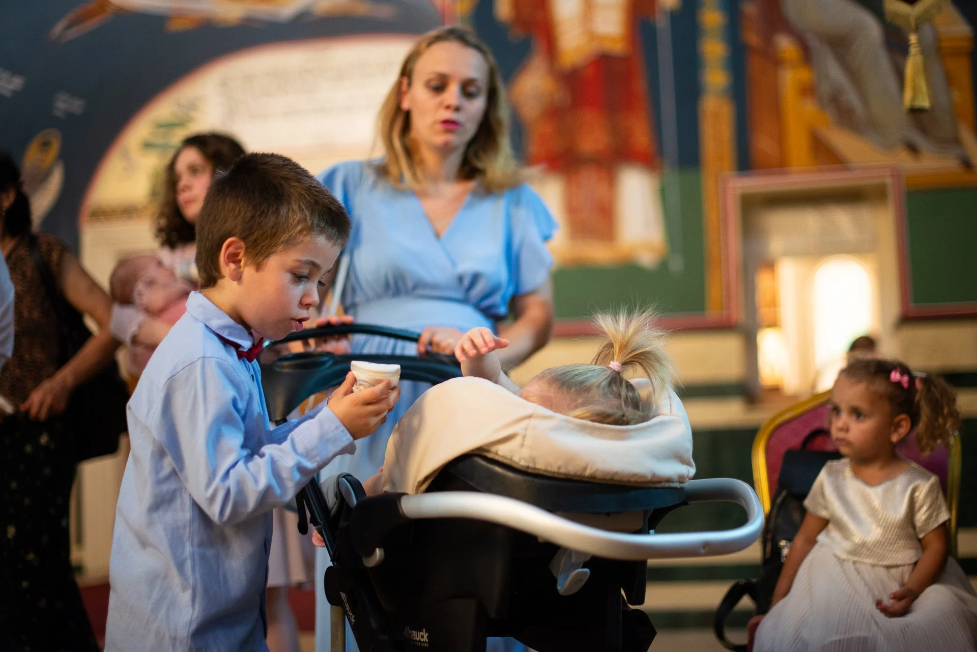 baietel care ii intinde o jucarie surorii lui care sta in carut