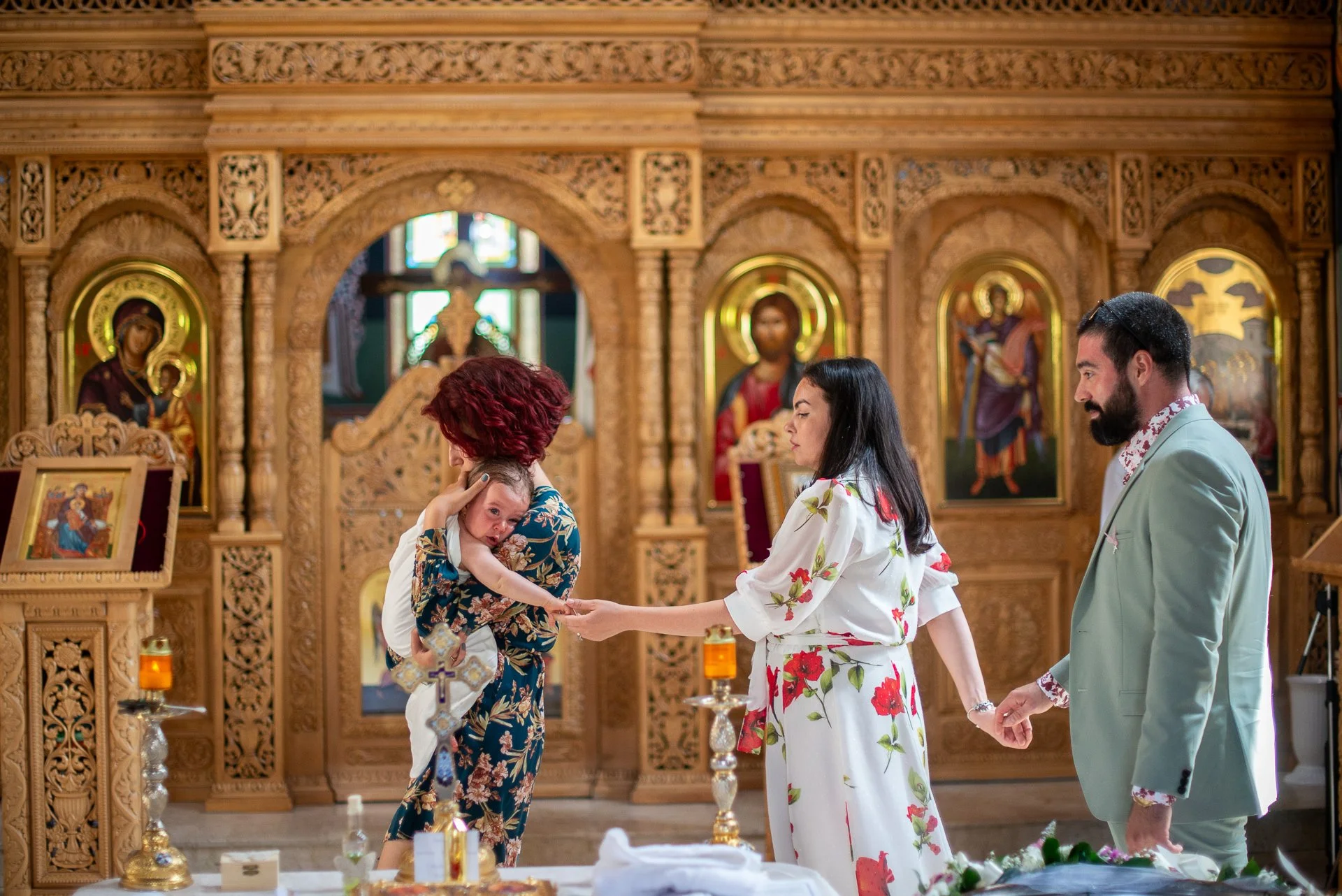 nasa cu bebelusu in brate si cu mama  se tin de maini in timpul slujbei botezului