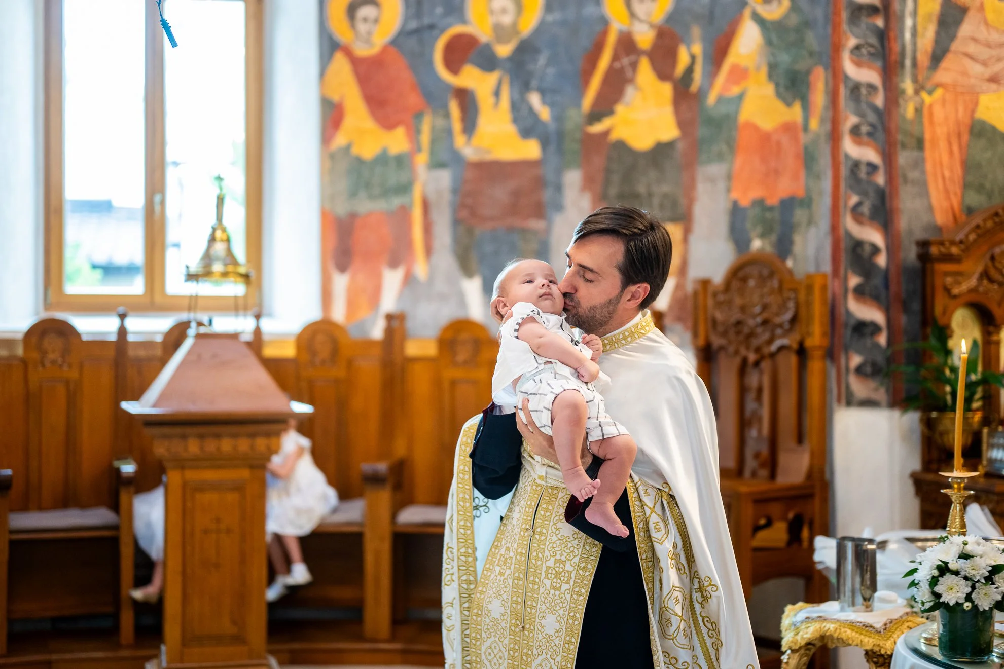 preotul ii ofera un sarut pe obraz bebelusului botezat