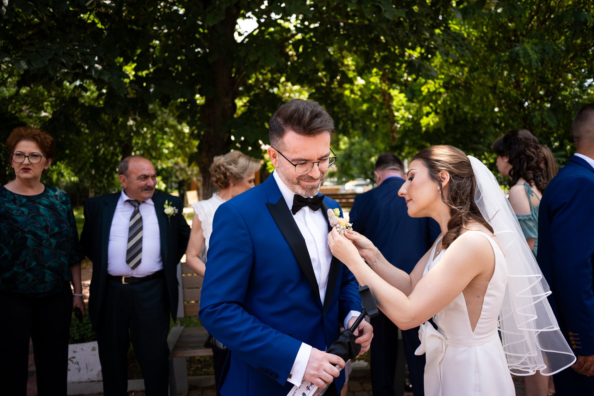 mireasa ii prinde cocarda mirelui in curtea bisercii inainte de slujba