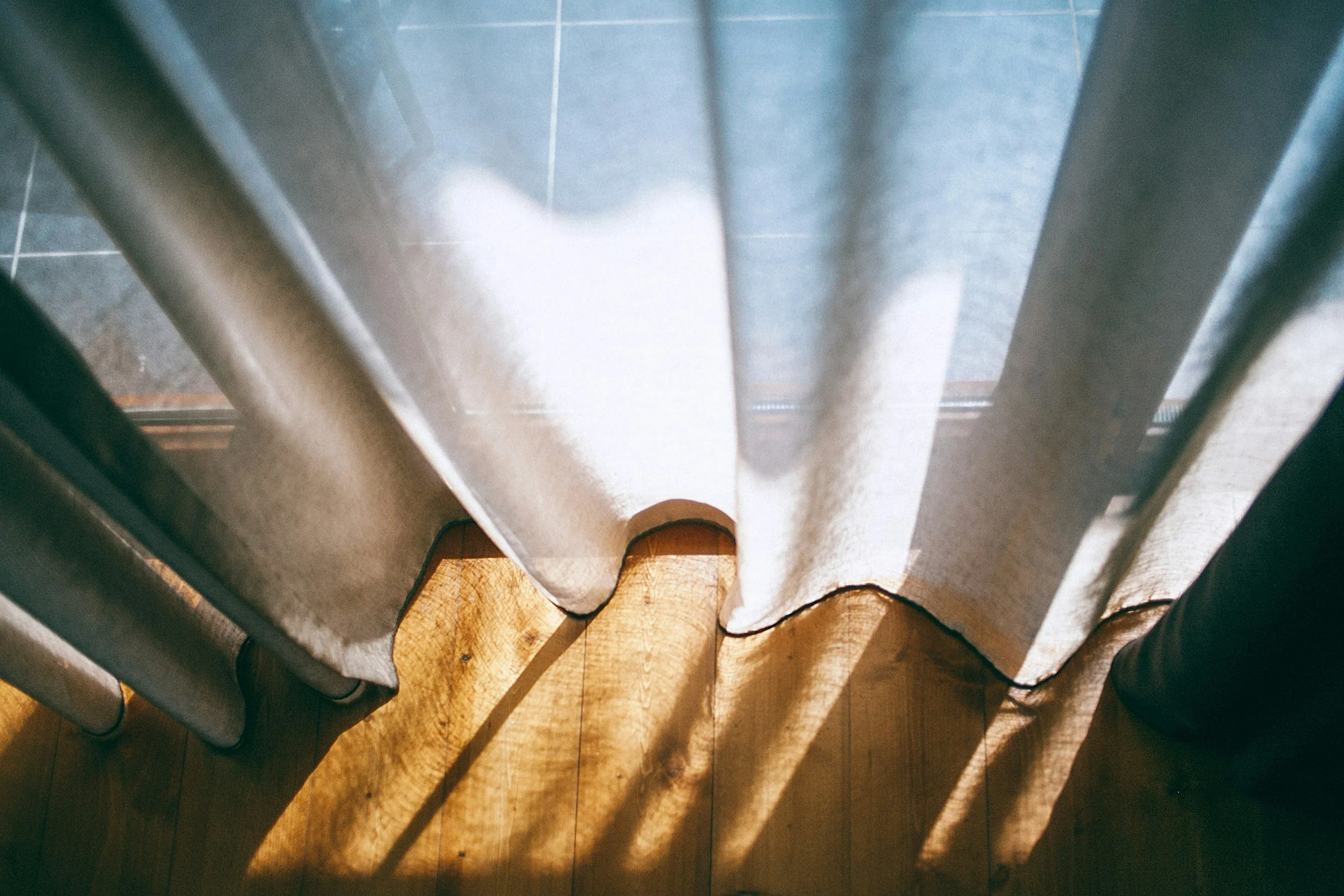 Solen tittar in genom gardiner och lyser upp trägolvet.