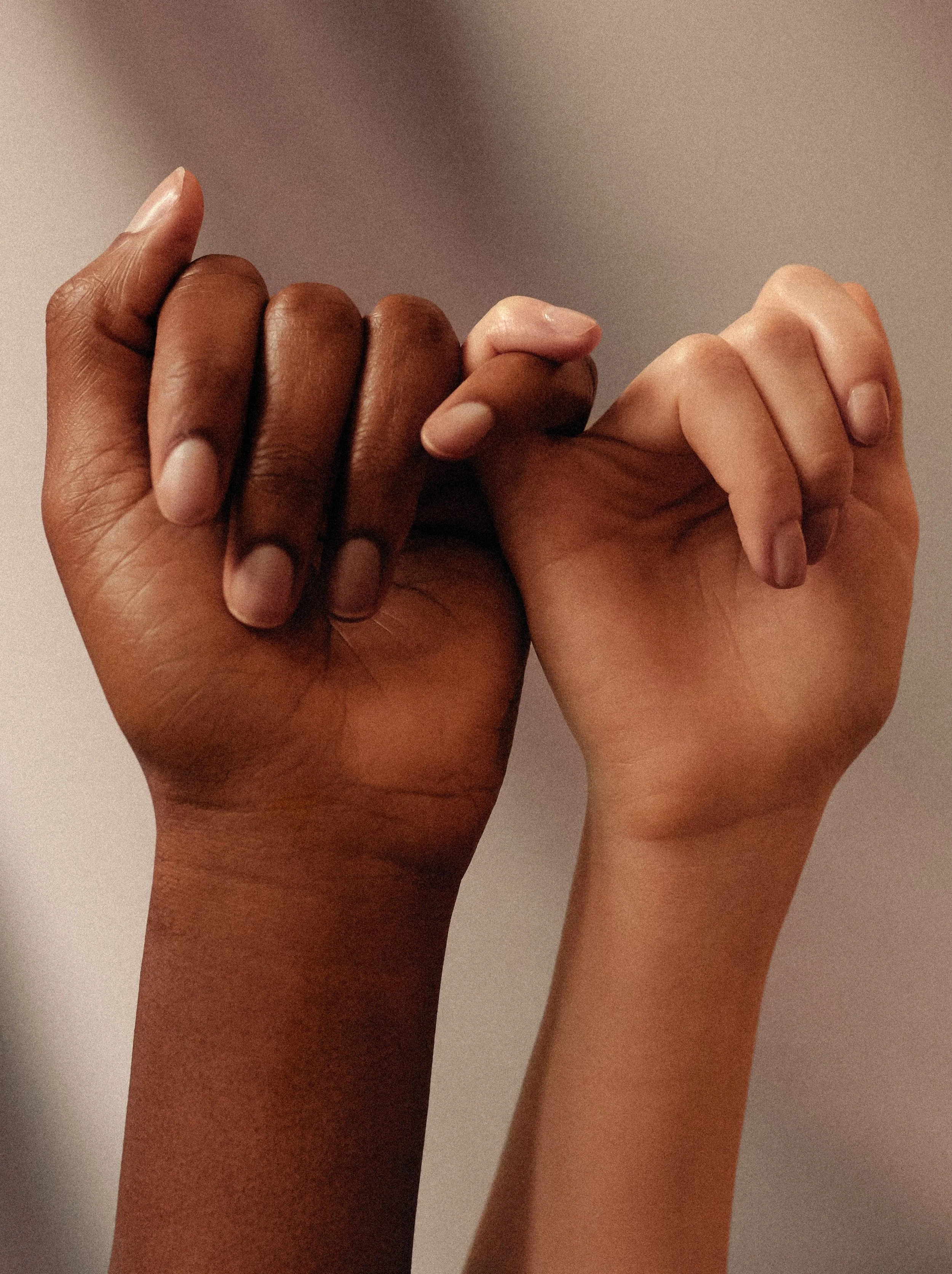Two hands with different, inclusive skin colours holding pinkies. A quiet gesture of connection and trust.