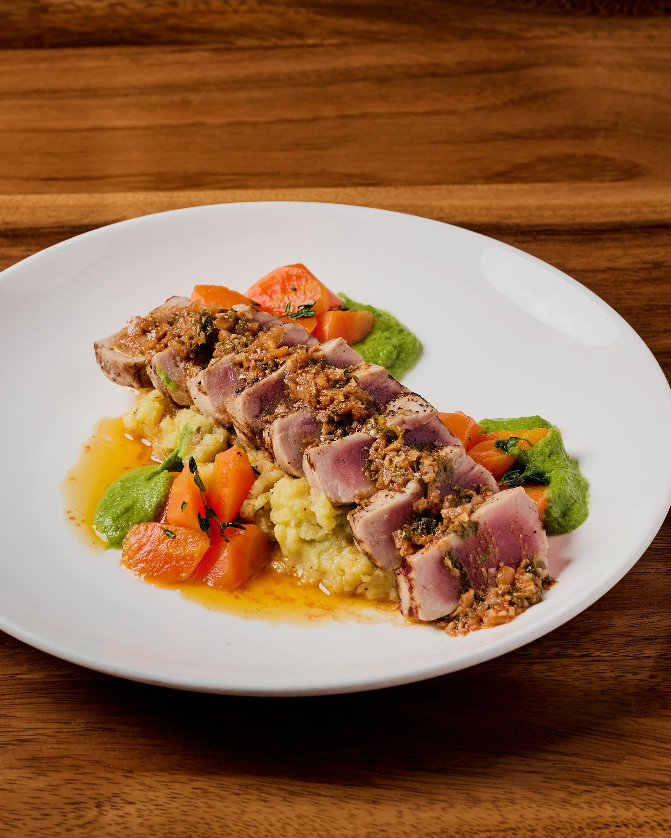 Seared tuna steak with chopped nuts and herbs, served over mashed potatoes with carrots, green pea mash, and sauce.