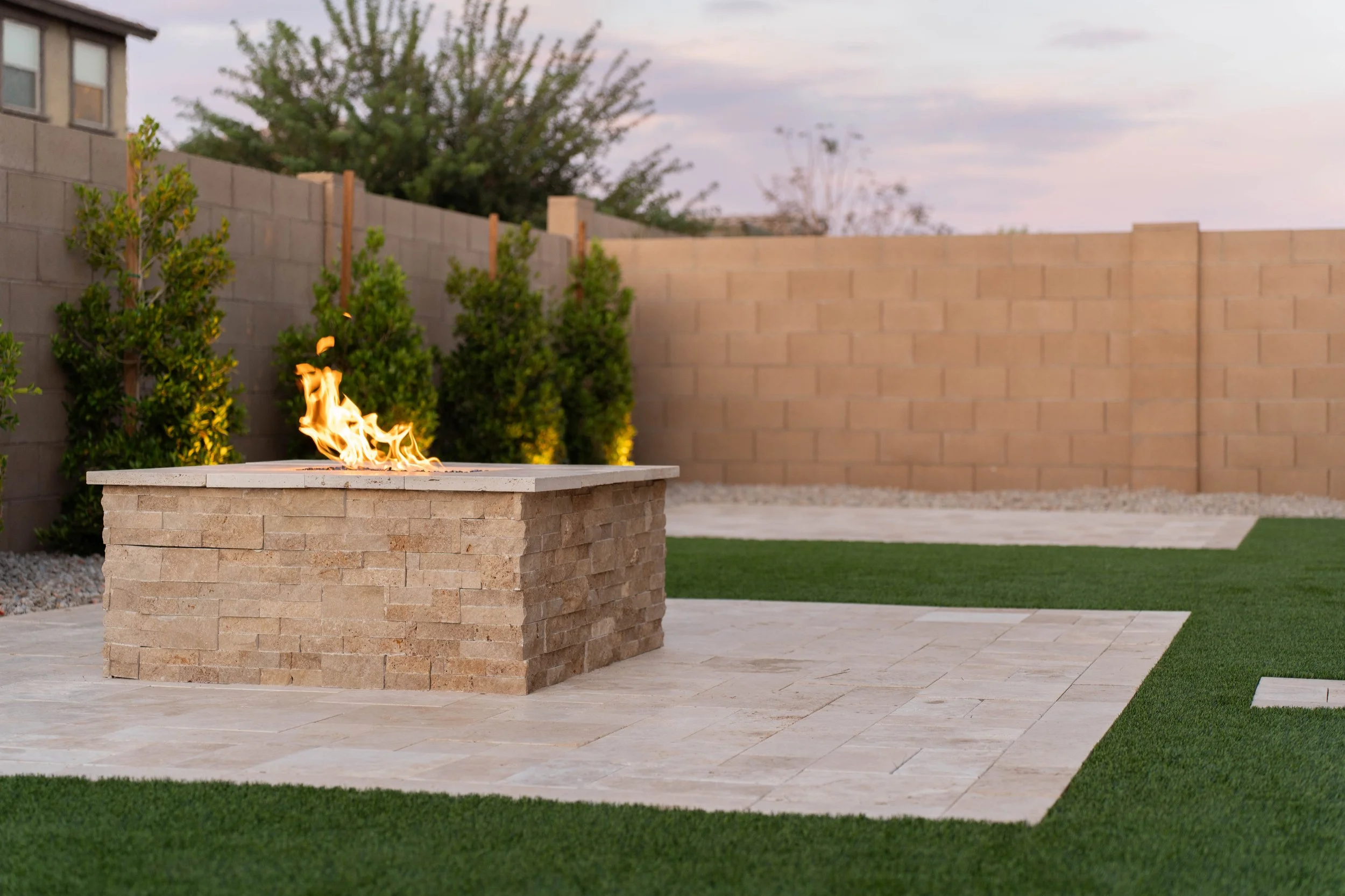 Custom fire pit, travertine, turf and trees installed at this local new build construction home near Queen Creek by Better Life Landscape & Design