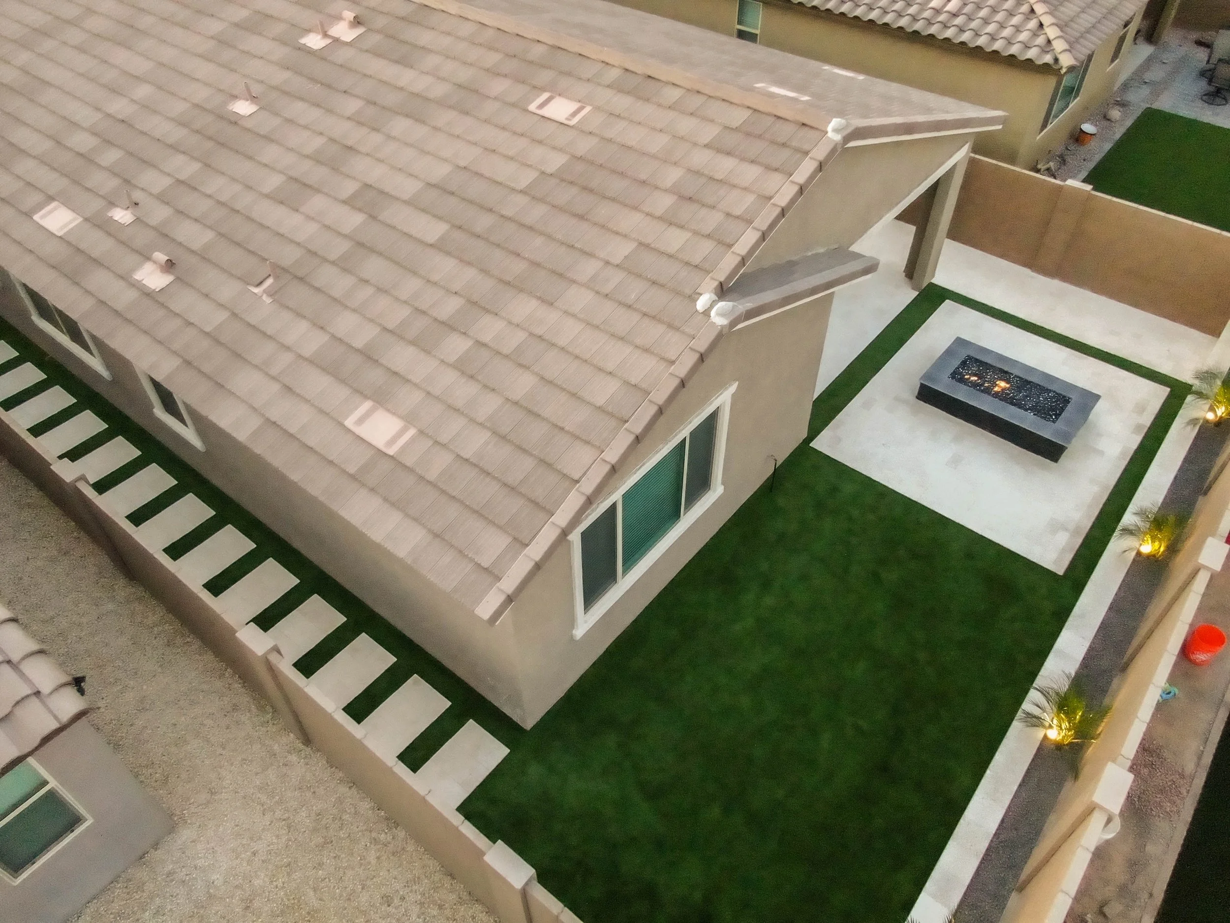 This residential backyard had many outdoor improvements, featuring tree planting, outdoor lighting, a custom-built fire pit, turf installation, and elegant travertine flooring.