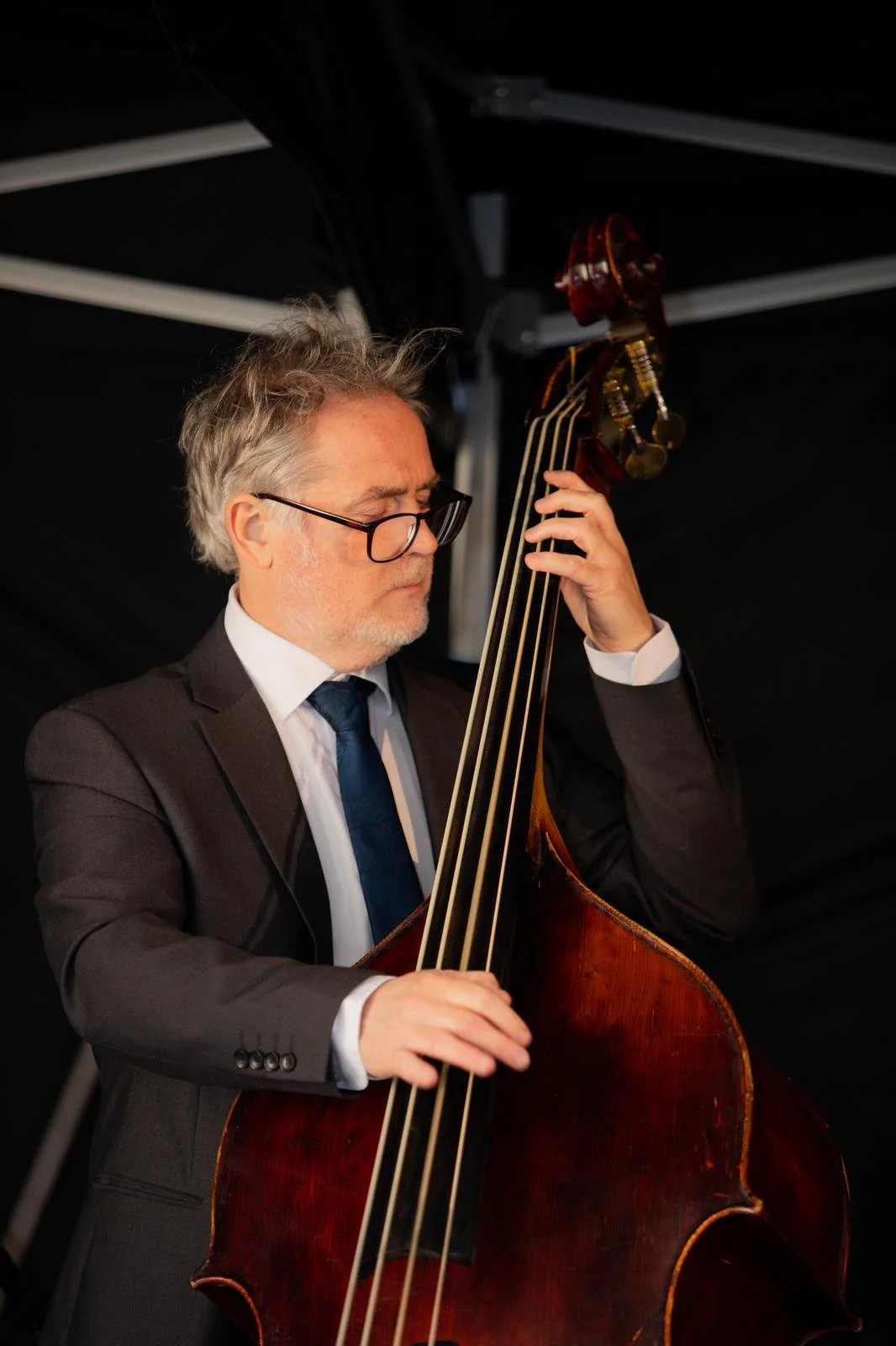 A man in a suit and tie playing a double bass in a performance setting.