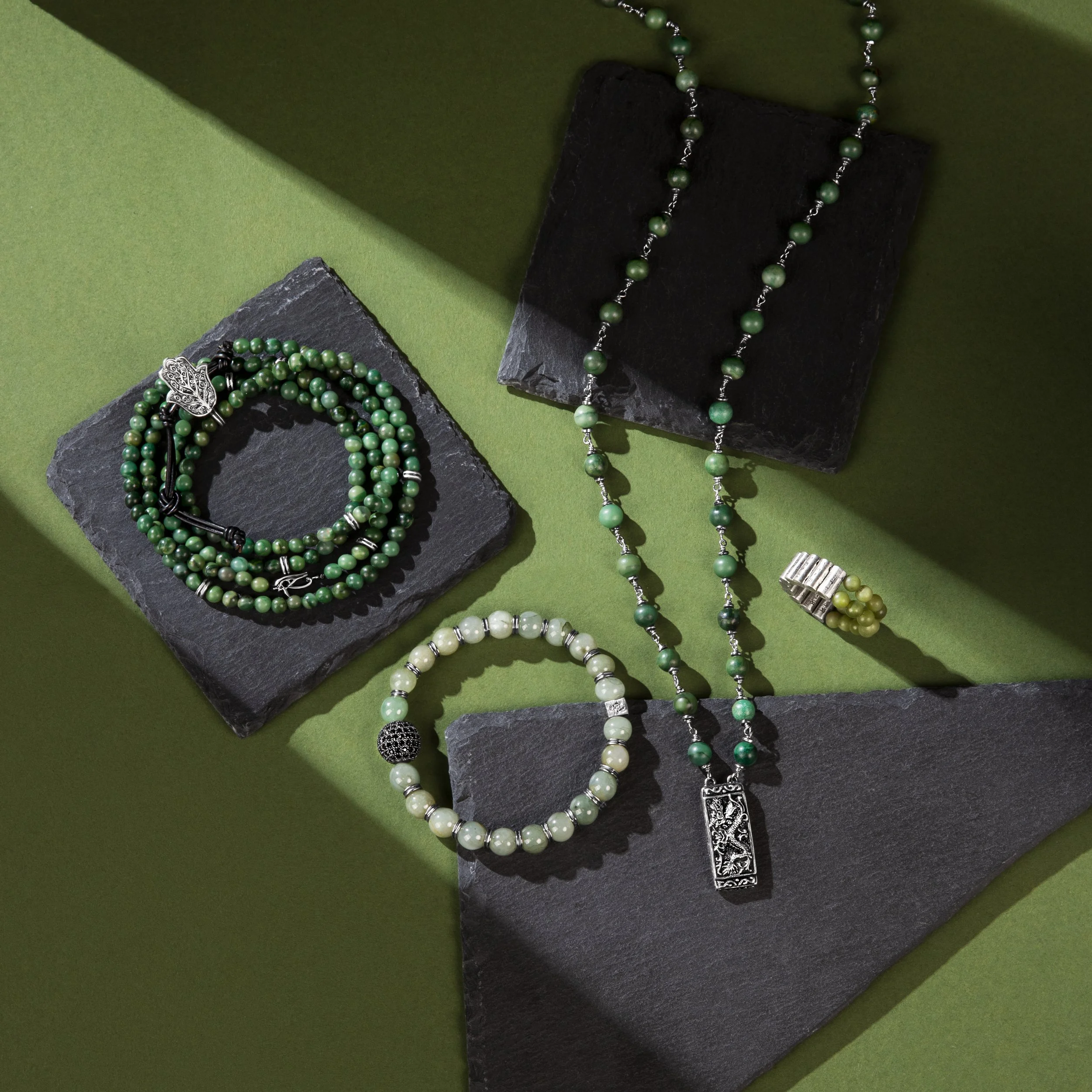 Collection of green jewelry including necklaces, bracelets, and rings displayed on black and green surfaces.