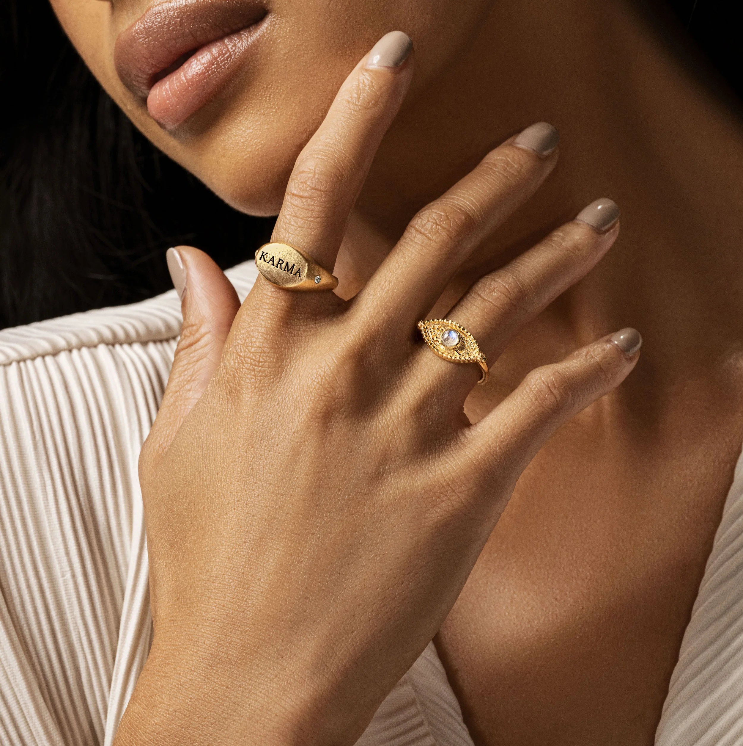 Close-up of a woman's hand with two gold rings, one with the word 'KARMA' and the other with a gemstone, near her lips and face.