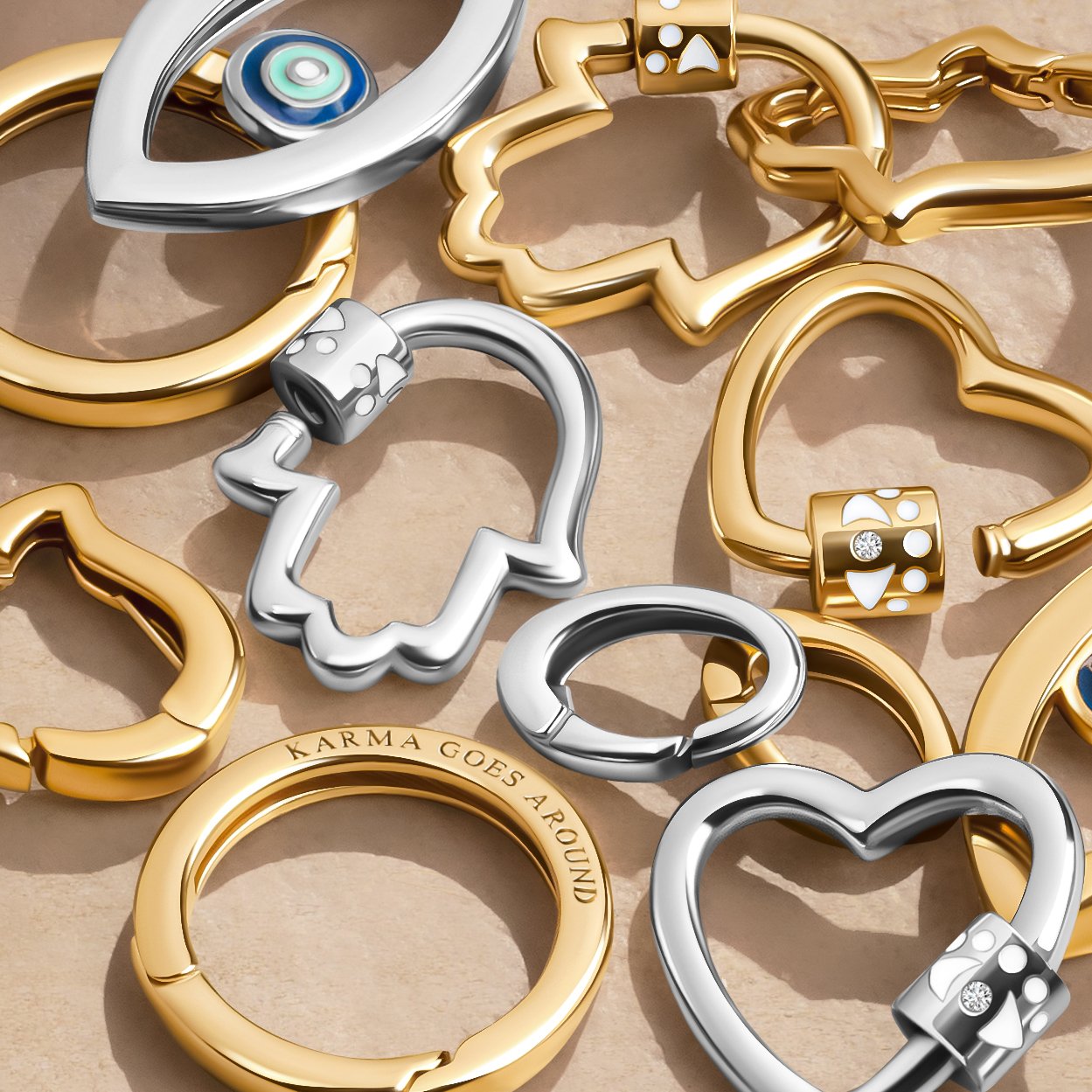 An assortment of metal keychain rings, including gold and silver hearts and loops, with some rings engraved or containing decorative dice designs, placed on a flat surface.