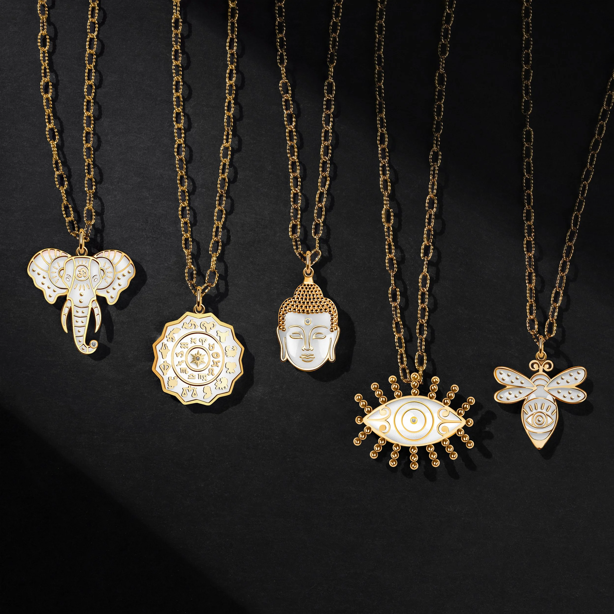 Five gold necklaces with various pendants, including an elephant, a circular design, a Buddha face, an eye design, and a bee with an eye.