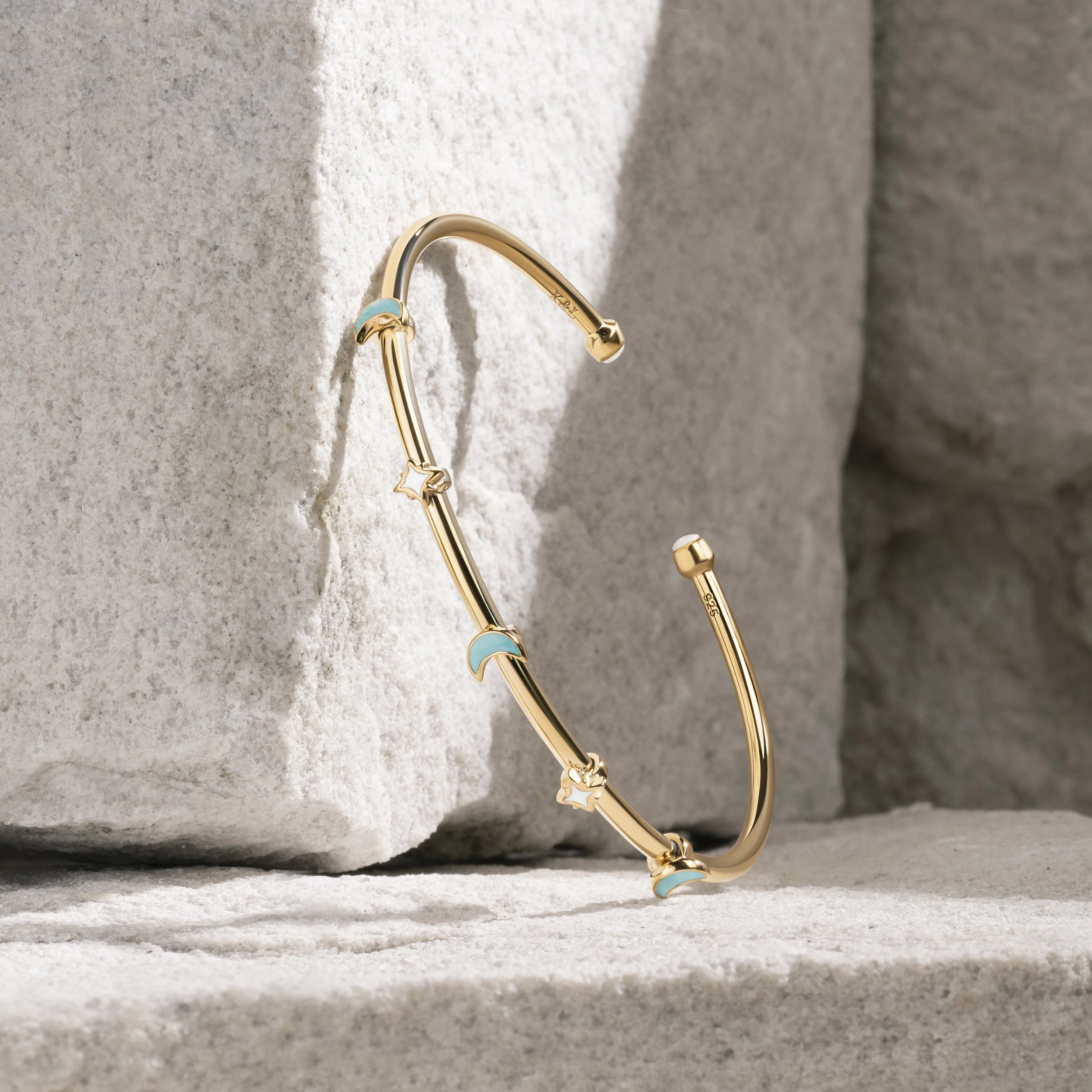 Gold bracelet with star, moon, and cloud charms, resting against a stone surface.