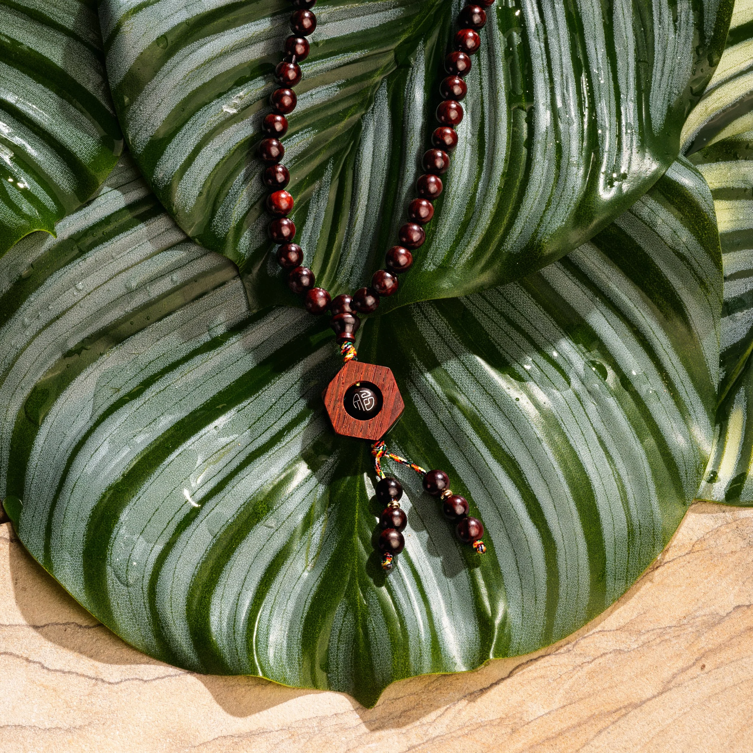 A beaded necklace with a wooden pendant lying on a large green tropical leaf.