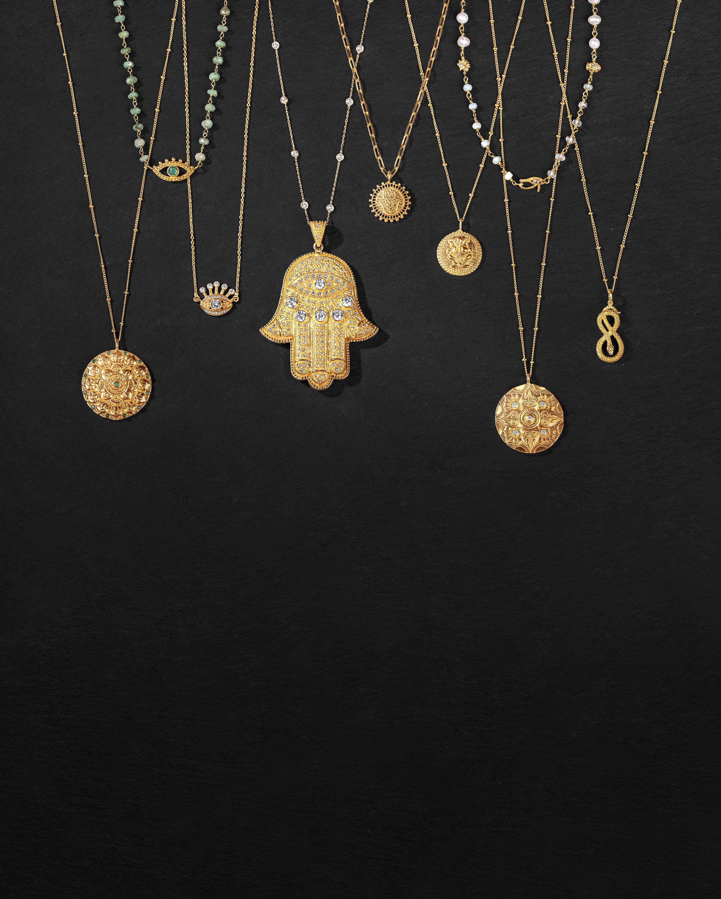 Collection of gold necklaces with various pendant designs laid out on a black background.