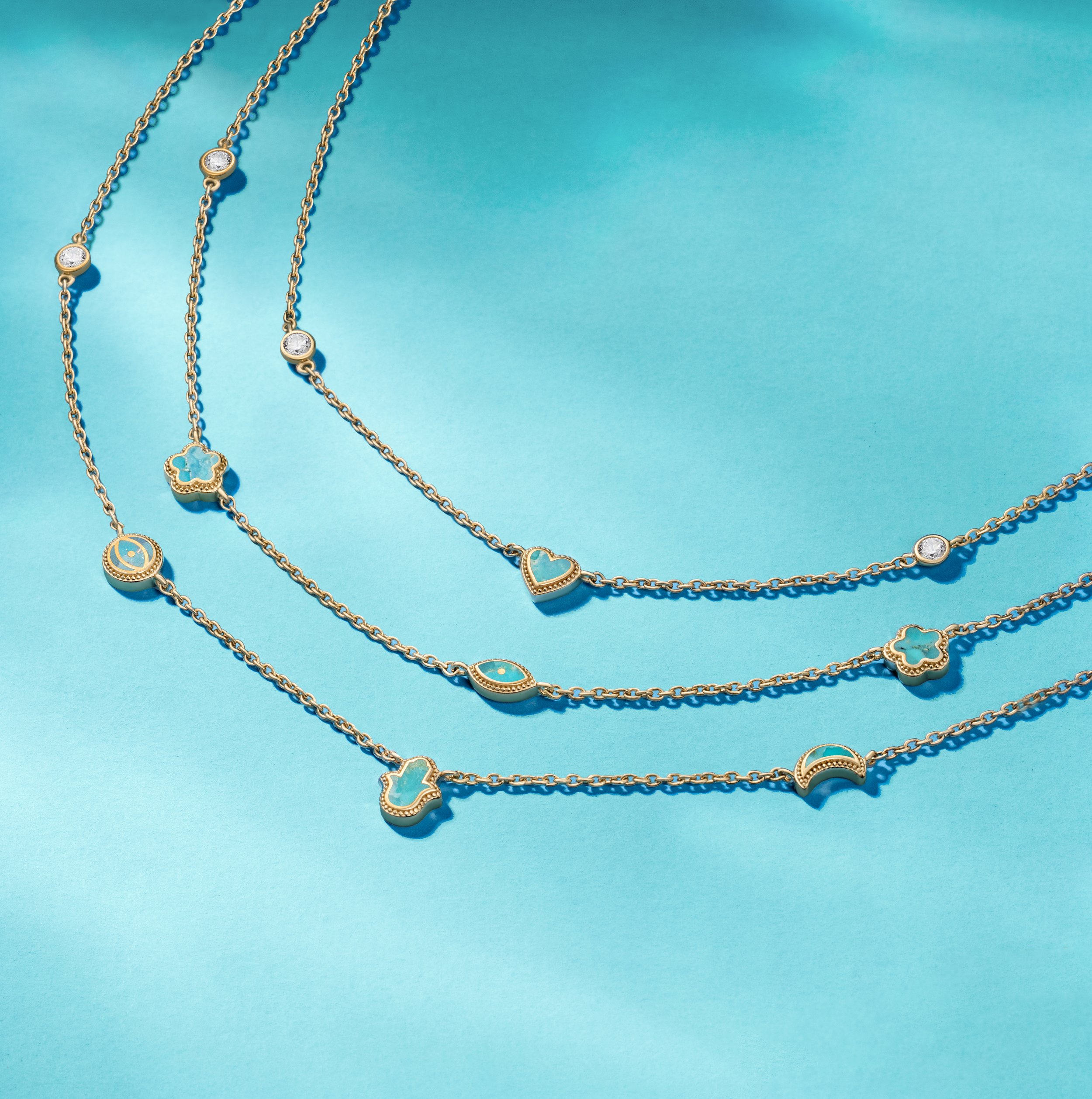 Four layered gold necklaces with various shaped charms, including hearts, stars, moons, and crescent moons, laid out on a blue background.