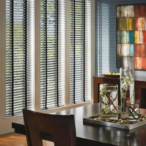 Dining room with large windows covered by white horizontal blinds, a dark wooden dining table with chairs, and a colorful abstract painting on the wall.