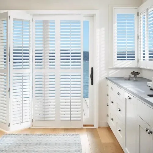 Bright kitchen with white shutters on windows and doors, white cabinets, silver handles, and a marble countertop.
