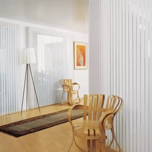 Minimalist living room with wooden chairs, a floor lamp, framed artwork, and vertical white blinds.
