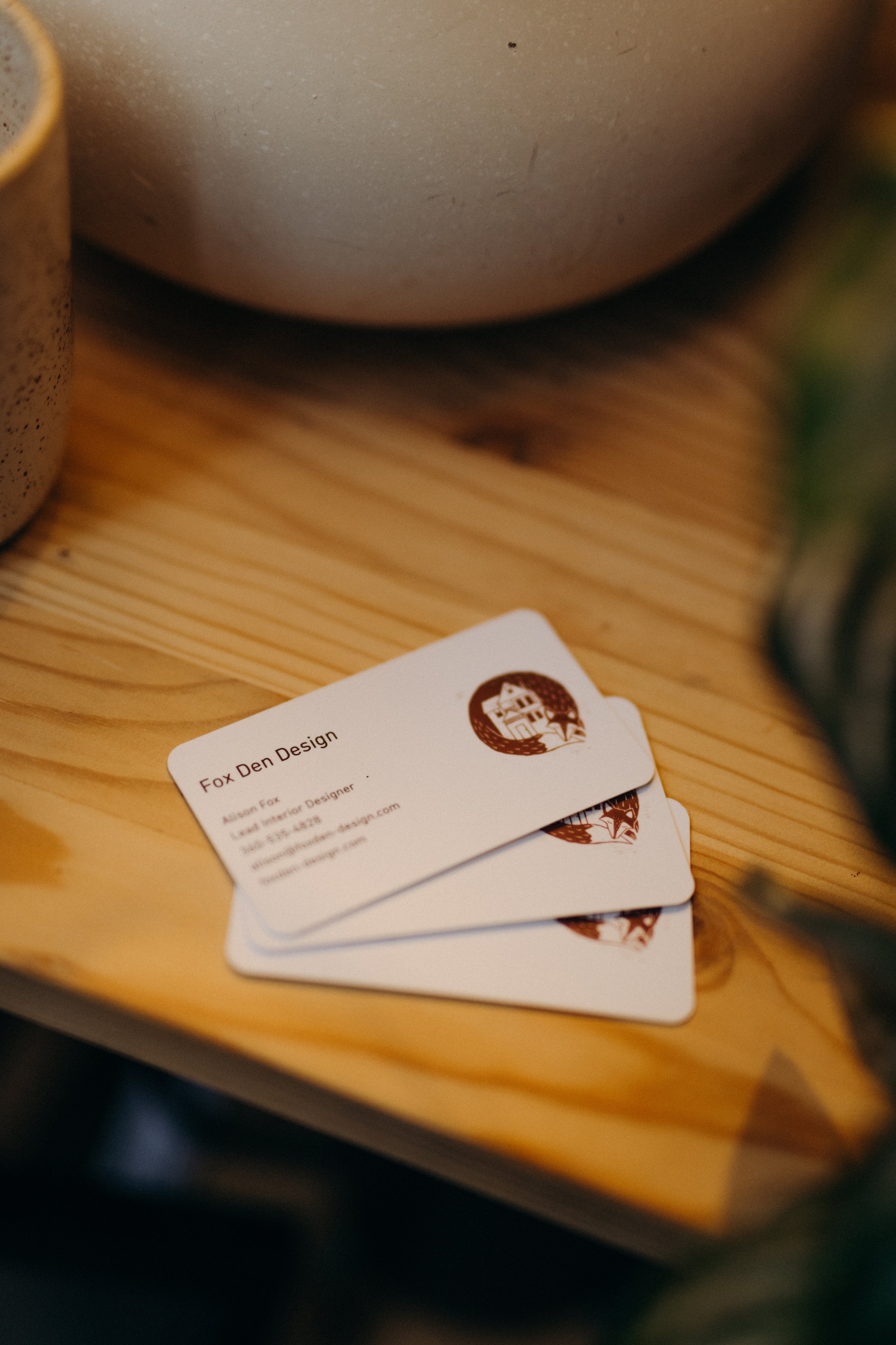 Business cards for Fox Den Design on a wooden surface.