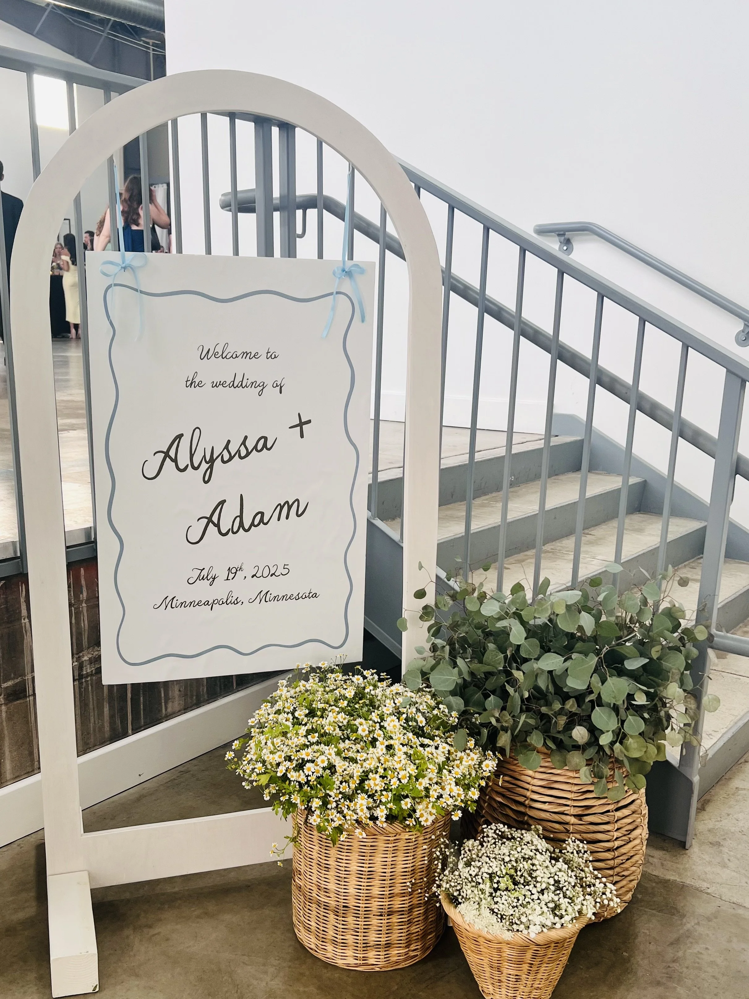 White arch, sign, and floral baskets provided by venue. Photo credit: Venue