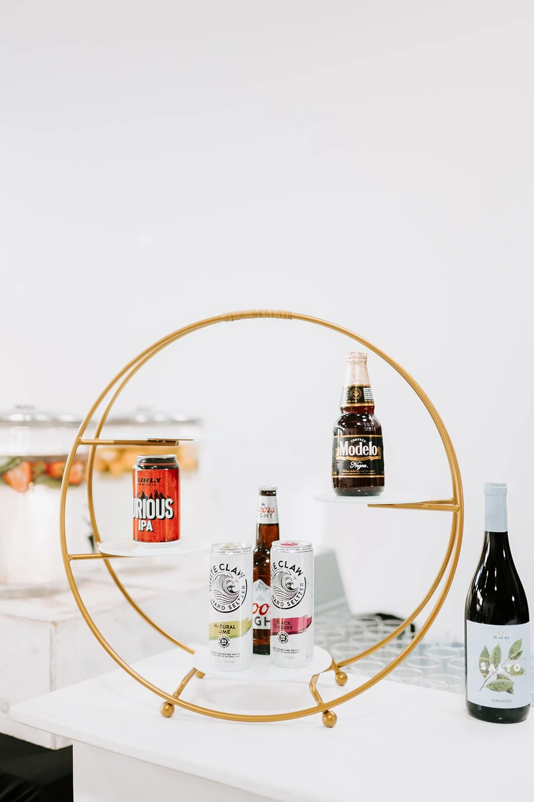 Beverage display with beer and seltzer cans on a circular gold metal stand, featuring multiple brands, on a white surface.