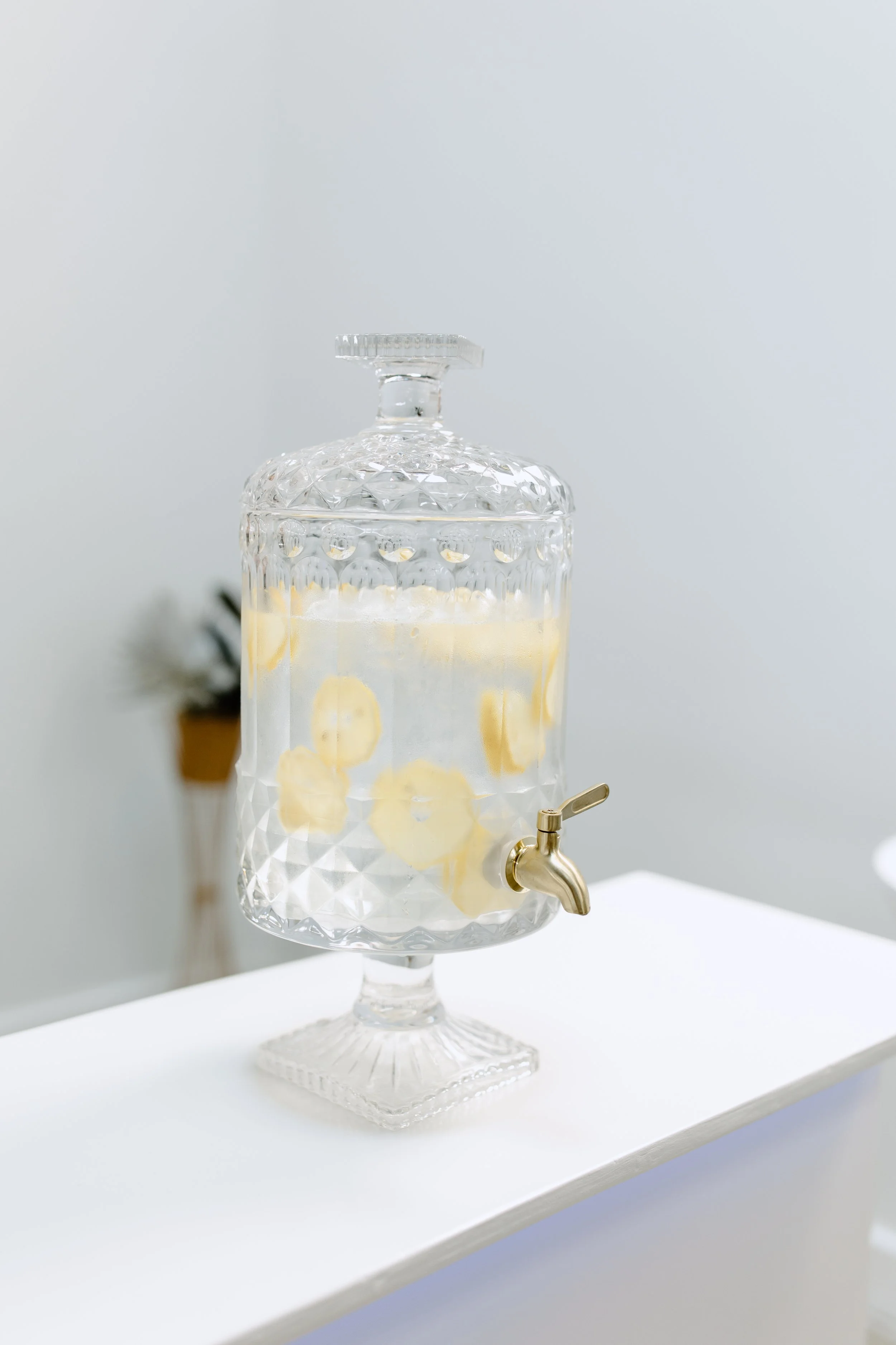 A glass beverage dispenser with a spigot, filled with lemon-infused water.