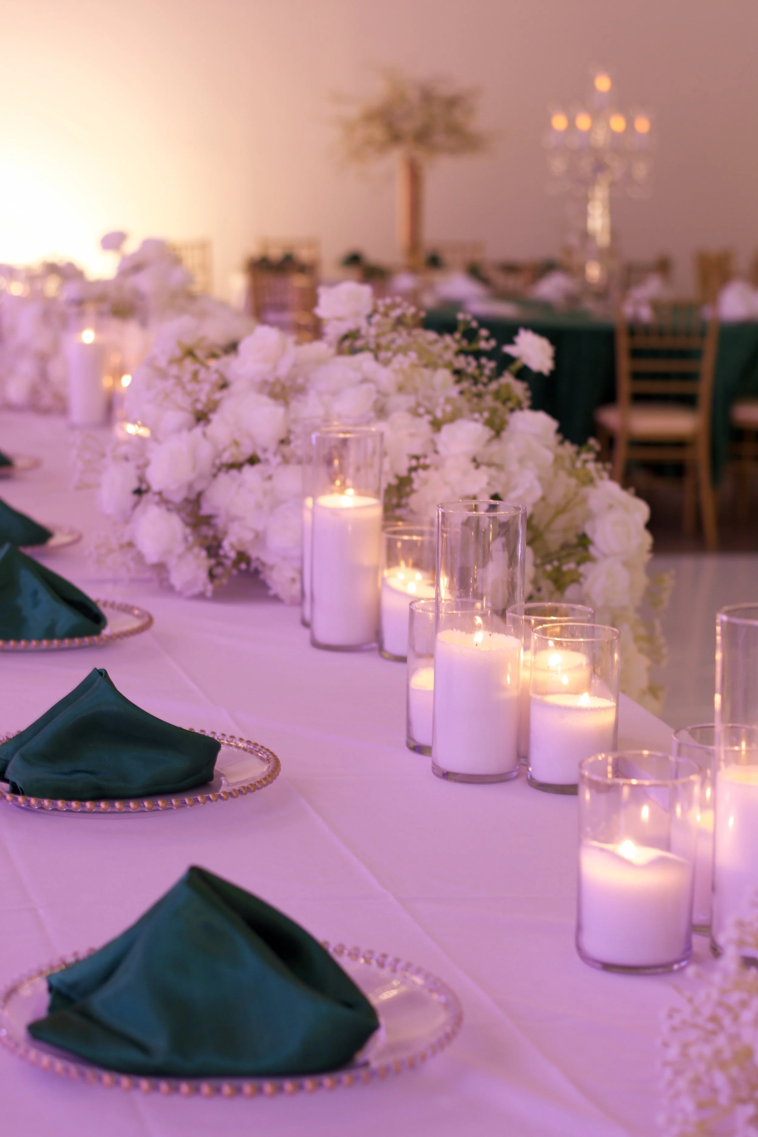 Dinner table setting with green napkins, gold chargers, candles, and a long banquet table for head table.