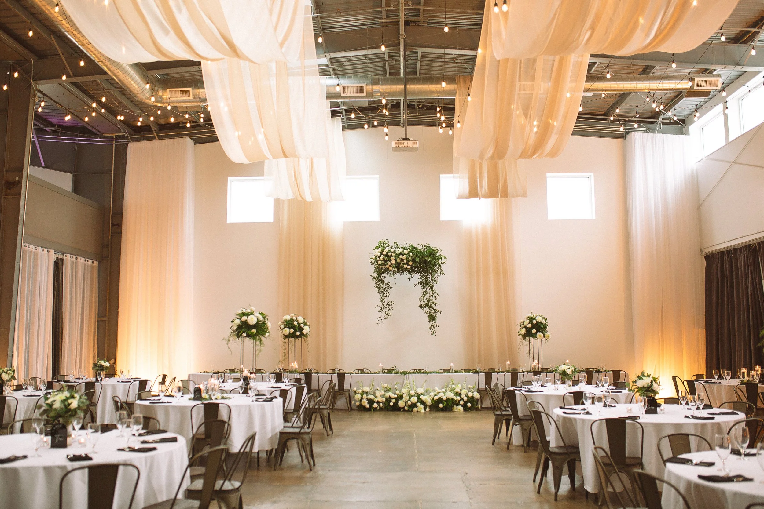 Large head table with white and green florals, and champagne colored 2 panel flat draping.