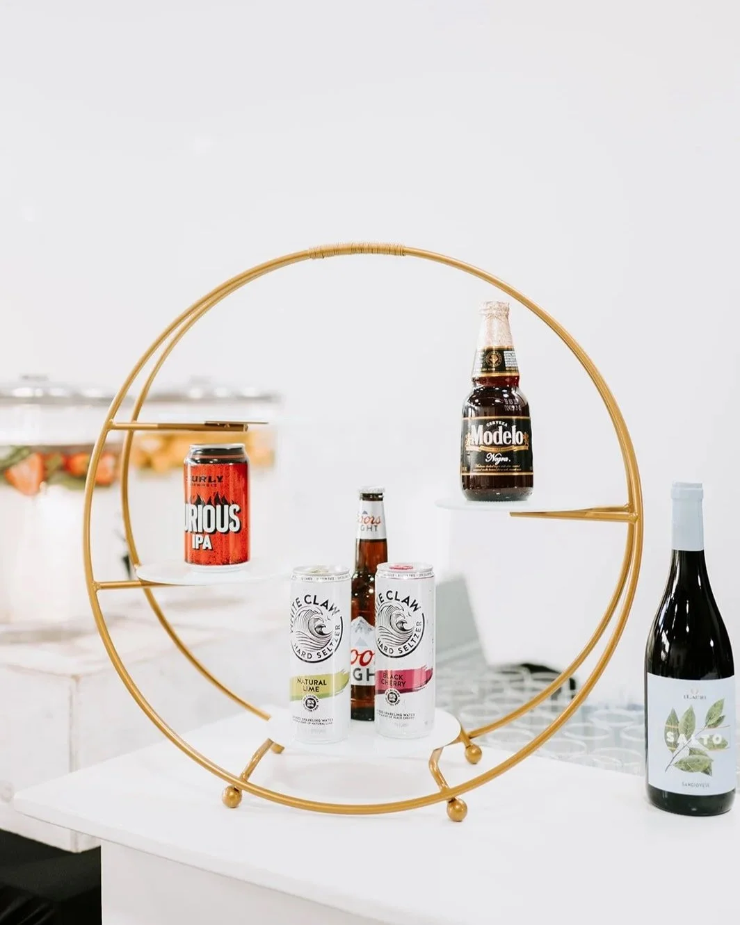 Beverage display with beer and seltzer cans on a circular gold metal stand, featuring multiple brands, on a white surface.