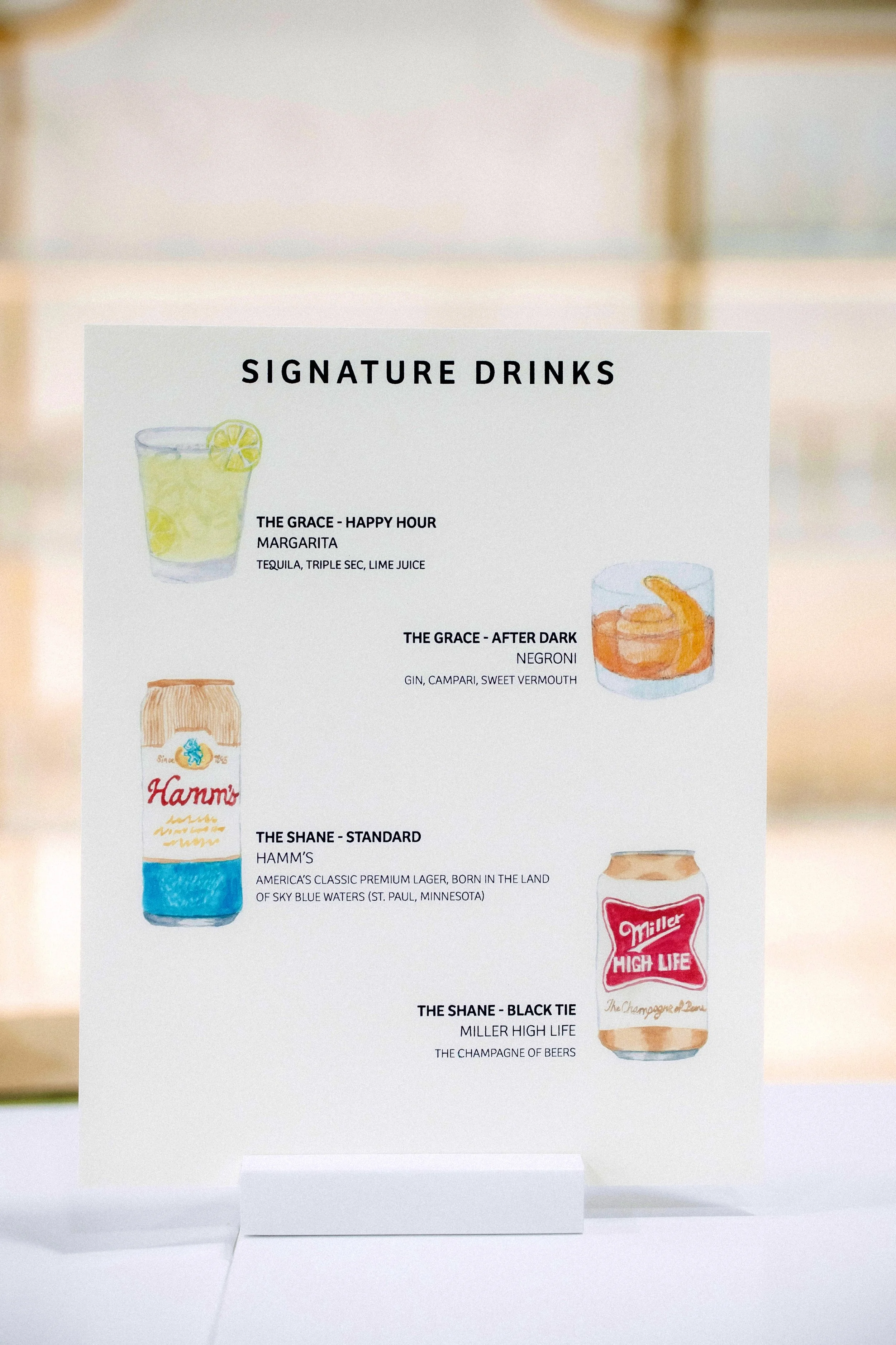 Menu displaying four signature drinks: "The Grace - Happy Hour Margarita" with tequila, triple sec, lime juice; "The Grace - After Dark Negroni" with gin, Campari, sweet vermouth; "The Shane - Standard Hamm's" described as a classic premium lager; "The Shane - Black Tie Miller High Life" referred to as the champagne of beers. Each drink has an accompanying illustration.