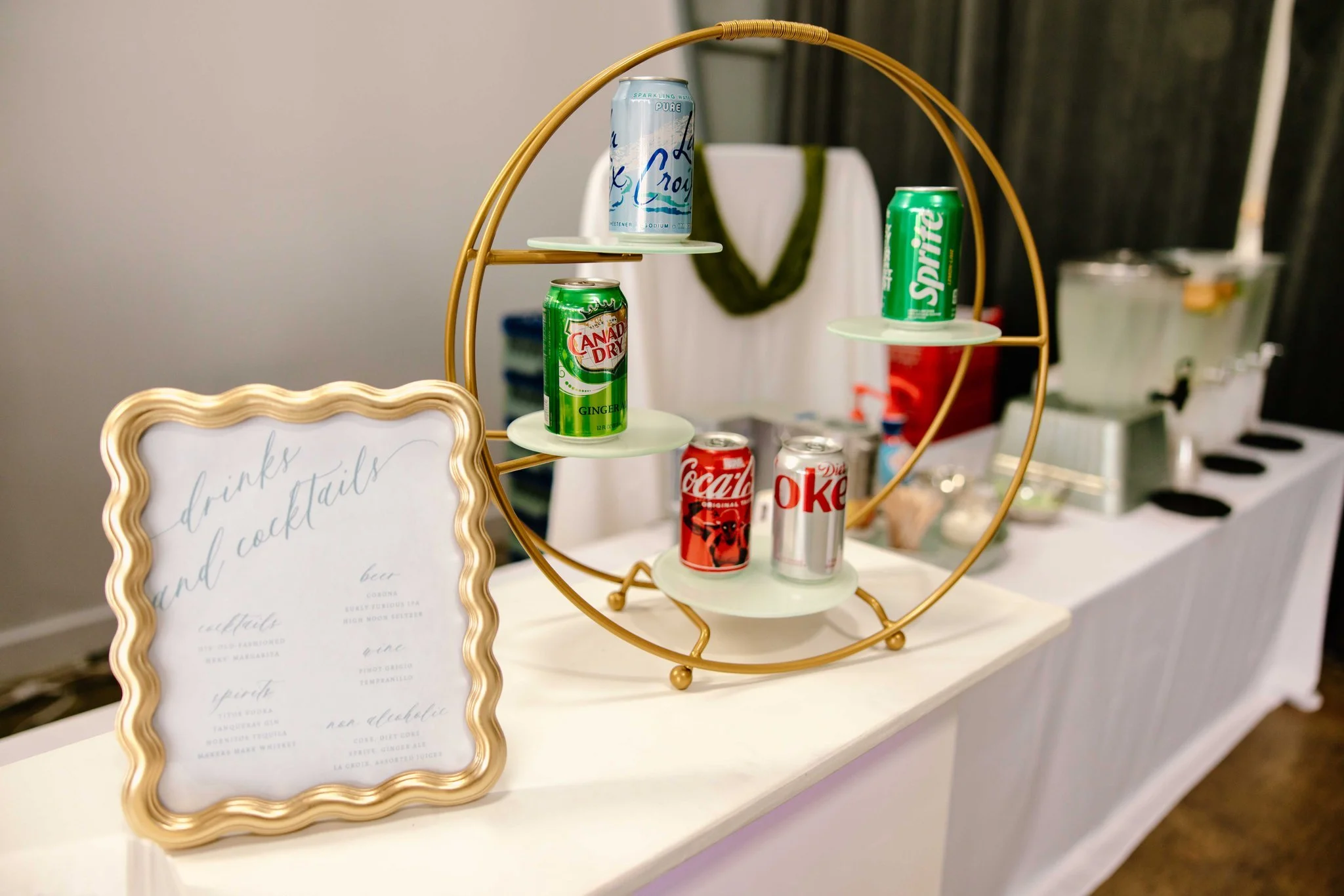 Table display with soda cans, LaCroix, Sprite, Canada Dry, Coca-Cola, Diet Coke, and framed drinks menu.