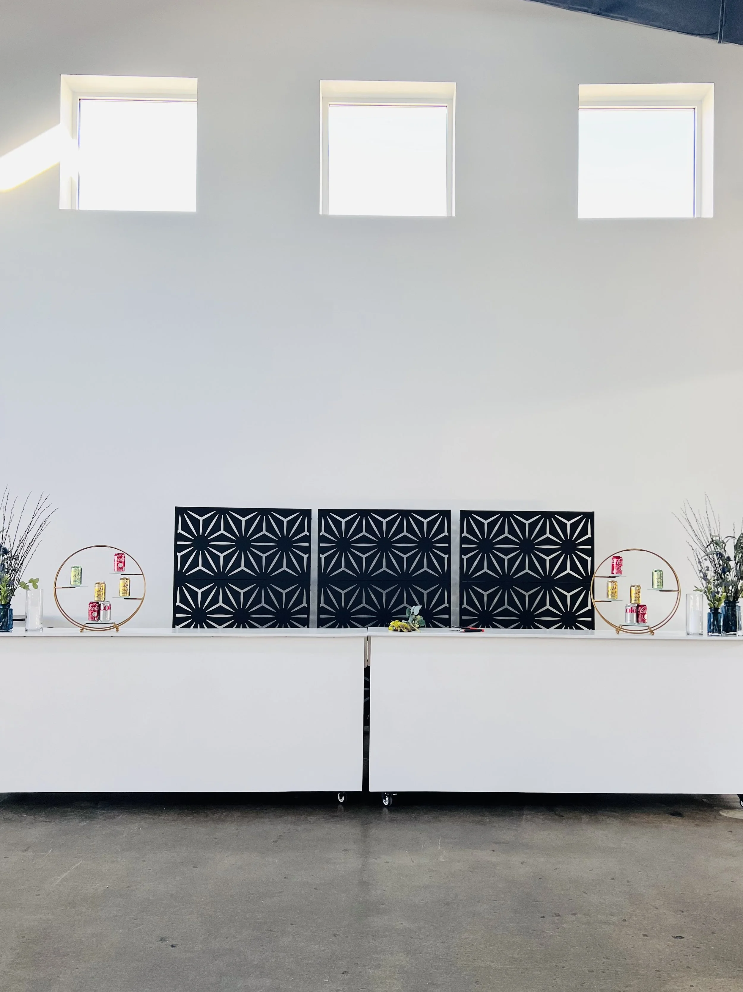 White bar with 3 tall black decorative metal frames as the backdrop, on white wall with tall windows.