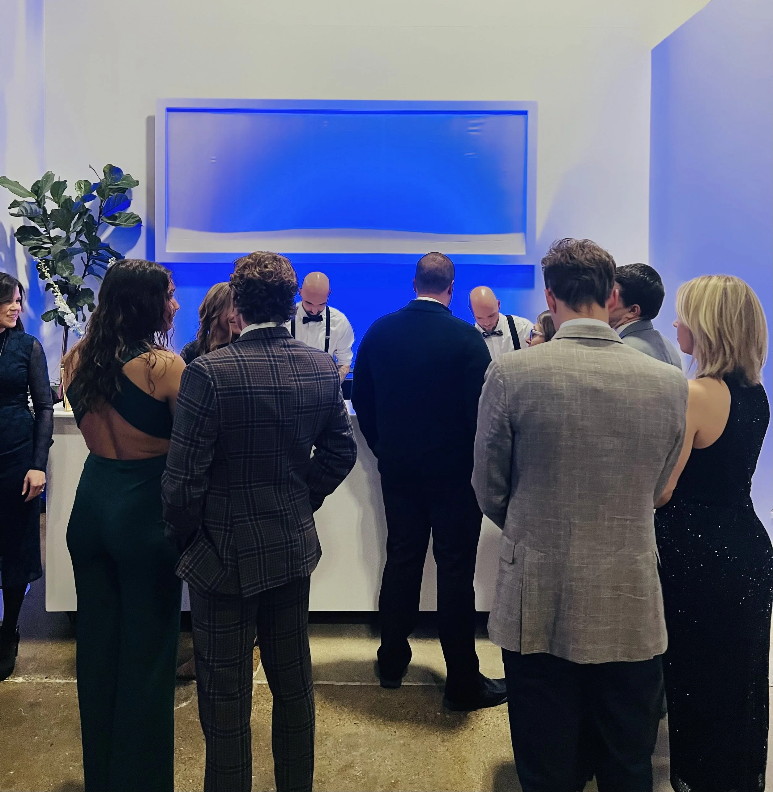 Bar with blue uplighting backdrop and guests in line waiting to order drinks
