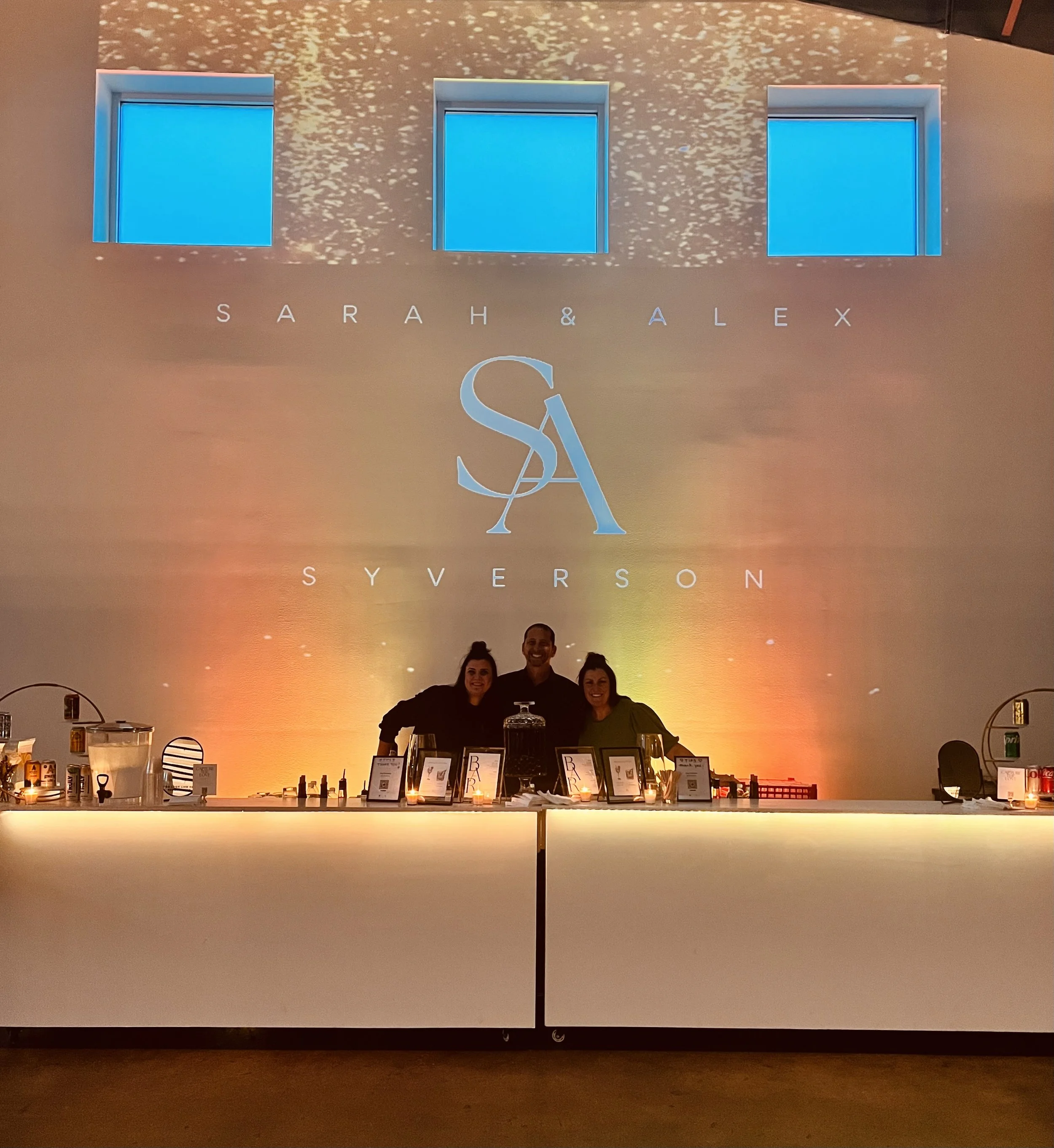 Image of 3 bartenders with projection mapping backdrop and colorful uplighting.