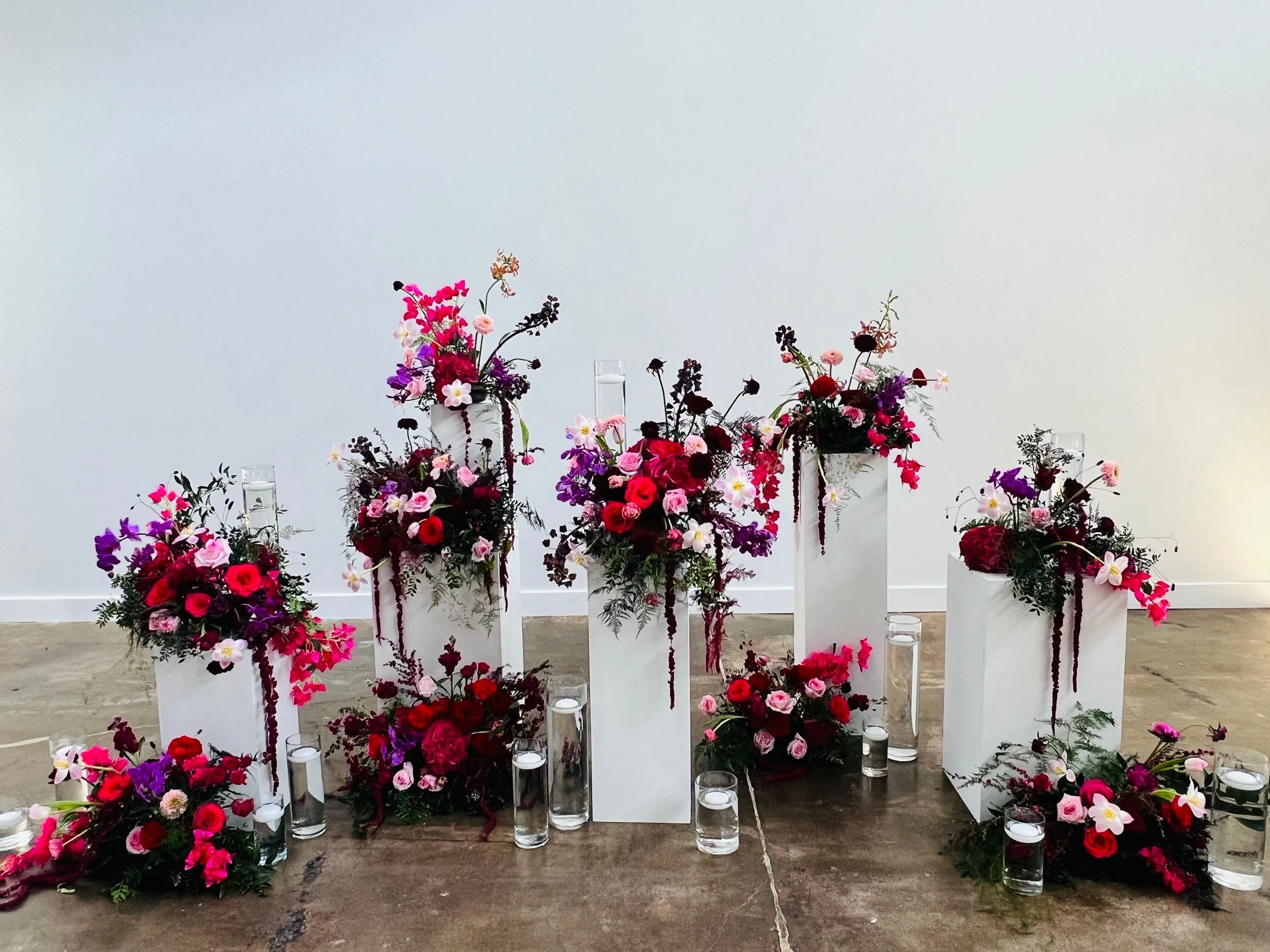 White pedestals, with vibrant colorful florals for photo backdrop area.