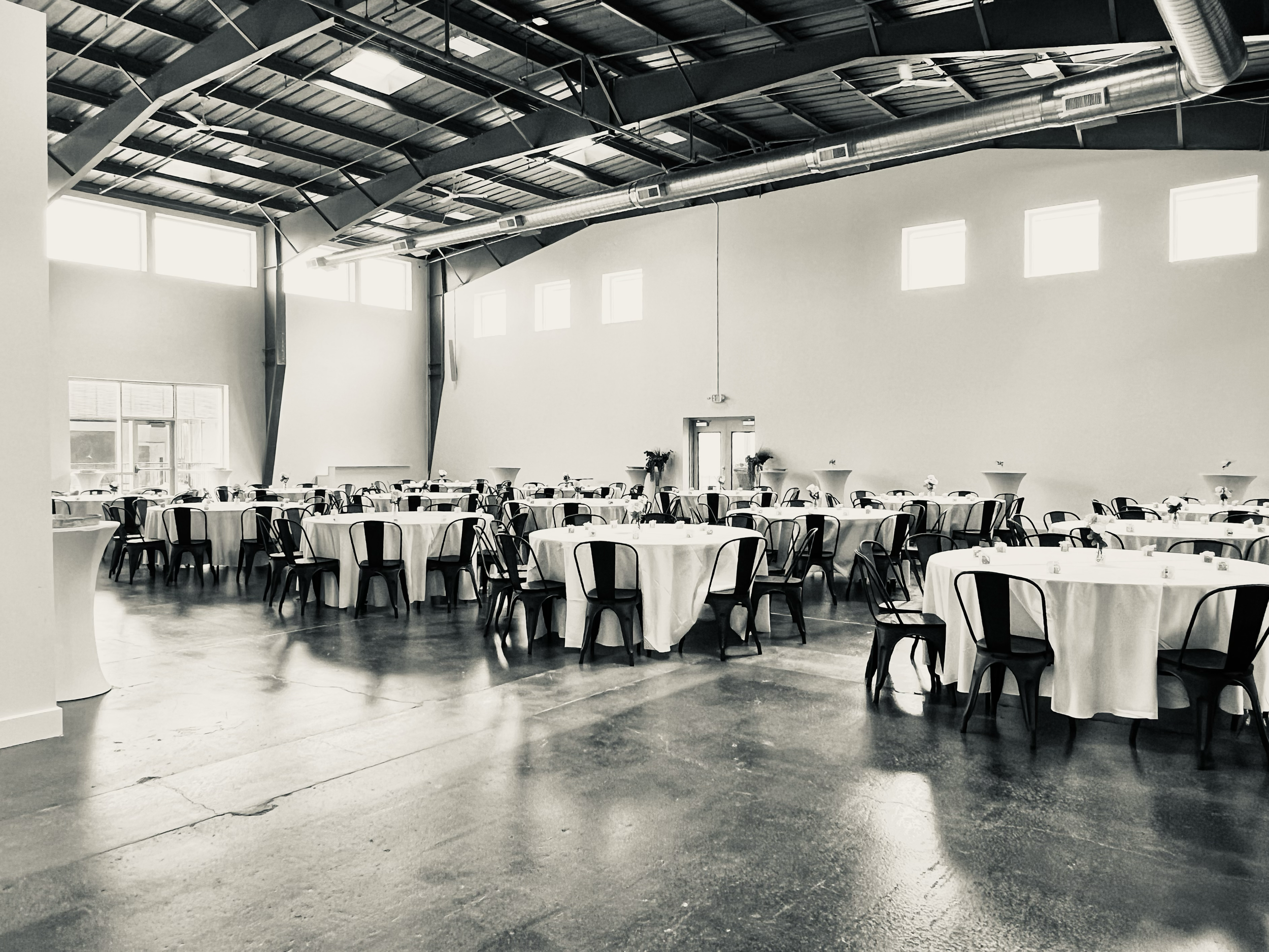 Front room of wedding venue that can host large groups with large banquet tables, and white floor length linens.