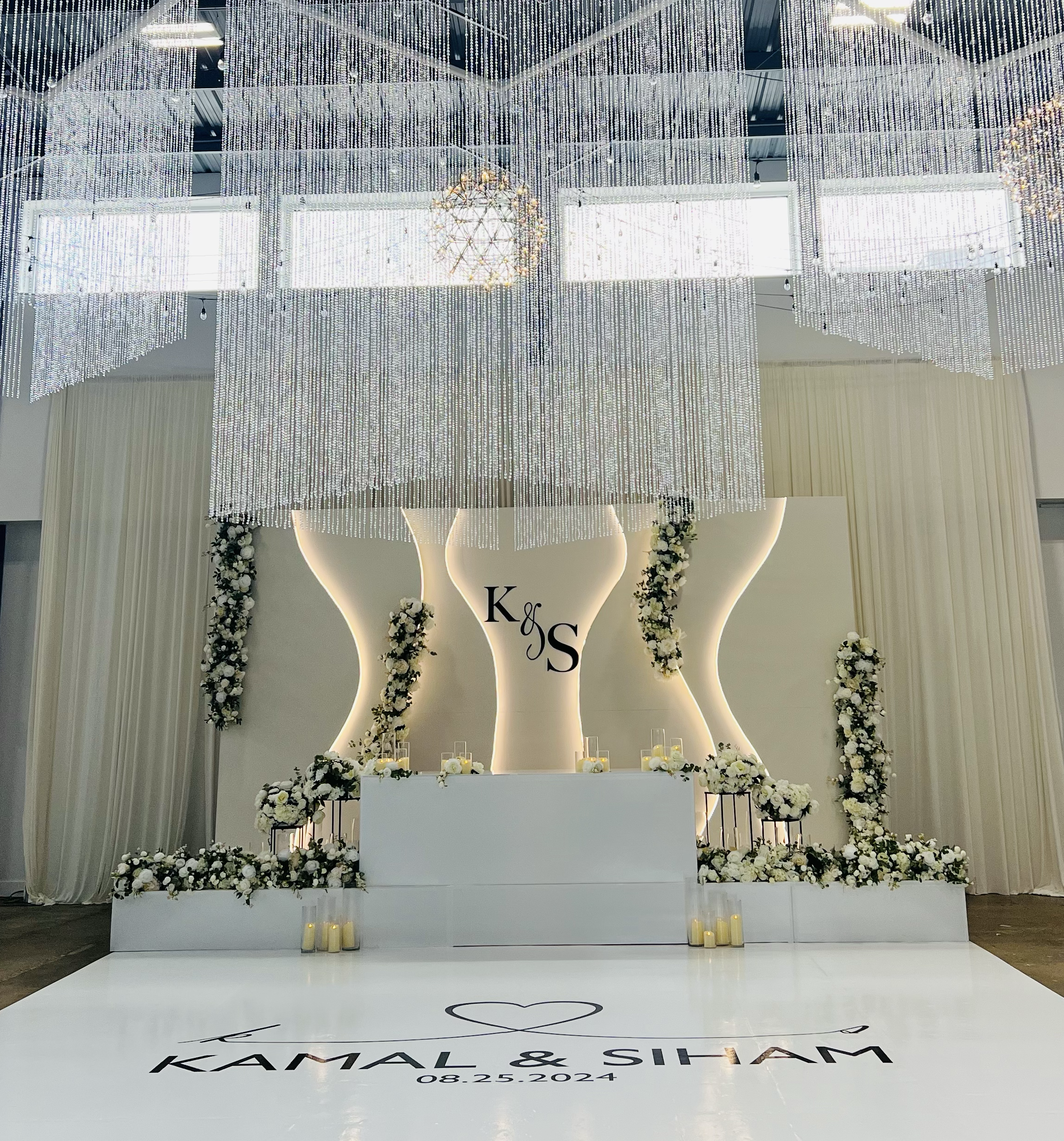 Beautiful white Nikkah ceremony backdrop with stage and lights.  Chandeliers and dance floor with vinyl wrapping and custom logo for the wedding couple.