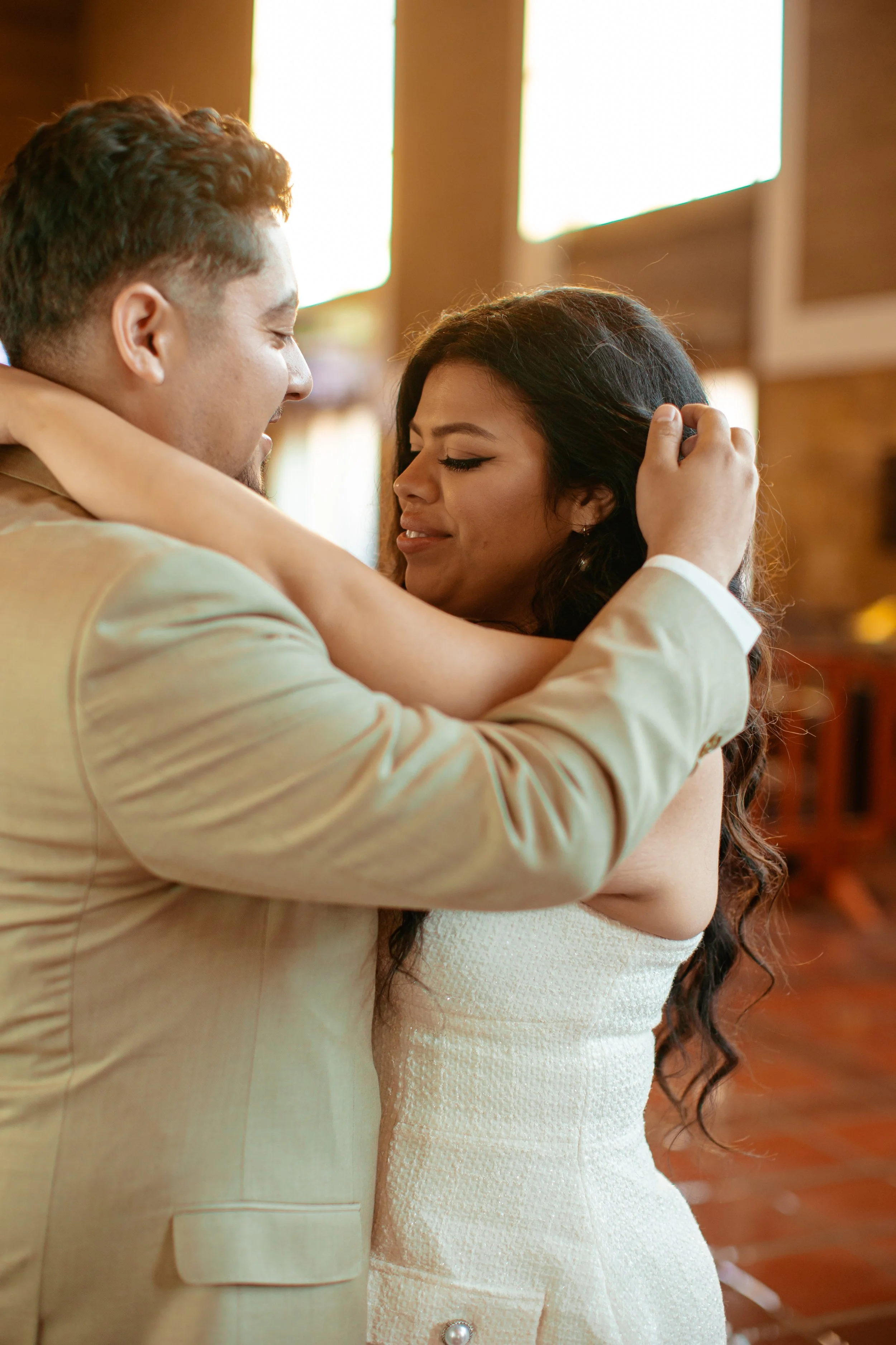 A couple dancing closely, smiling and holding each other inside a warmly lit room.