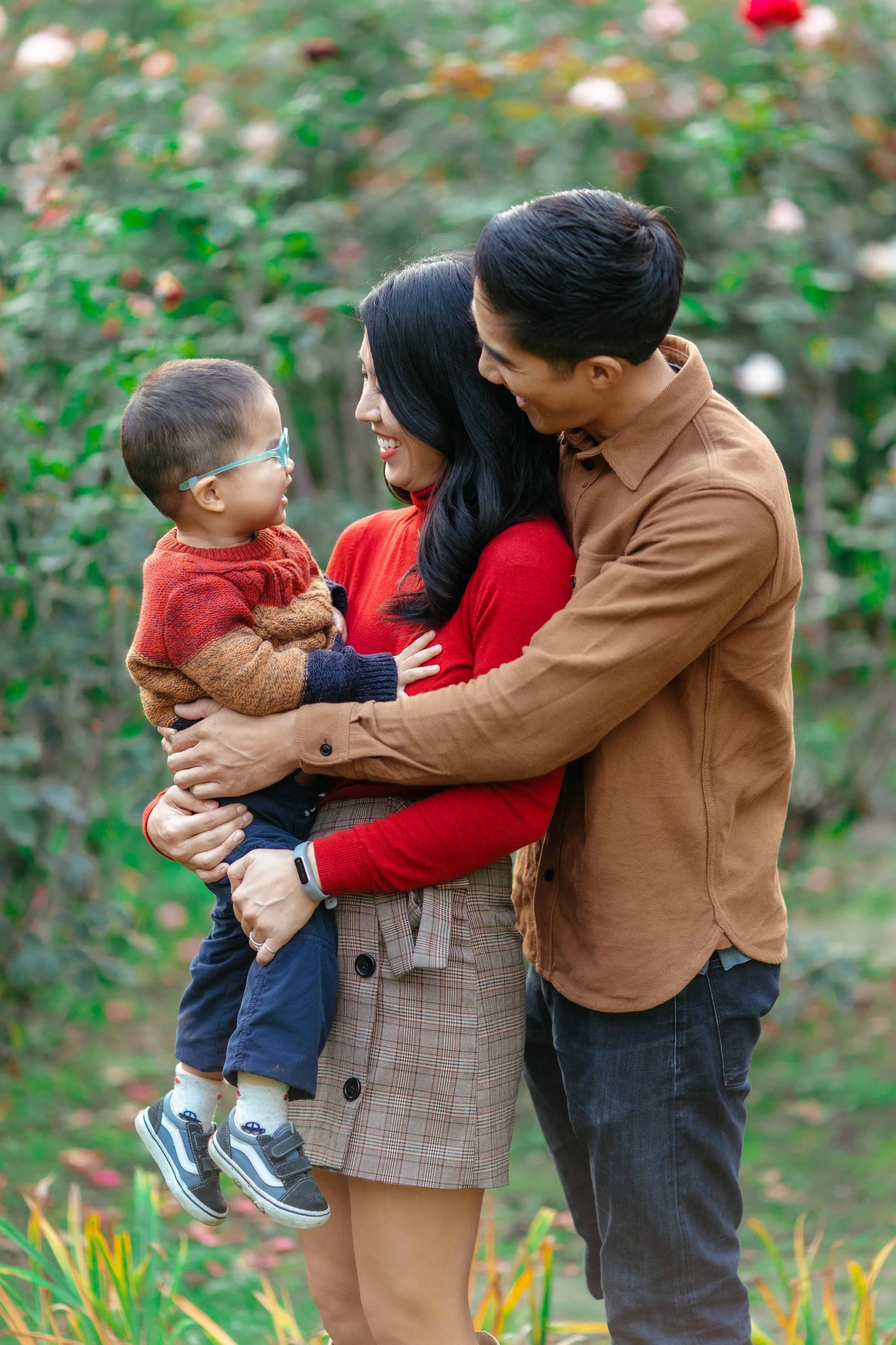 A happy family with a woman, a man, and a young boy outdoors in a garden, all smiling and happily looking at each other.