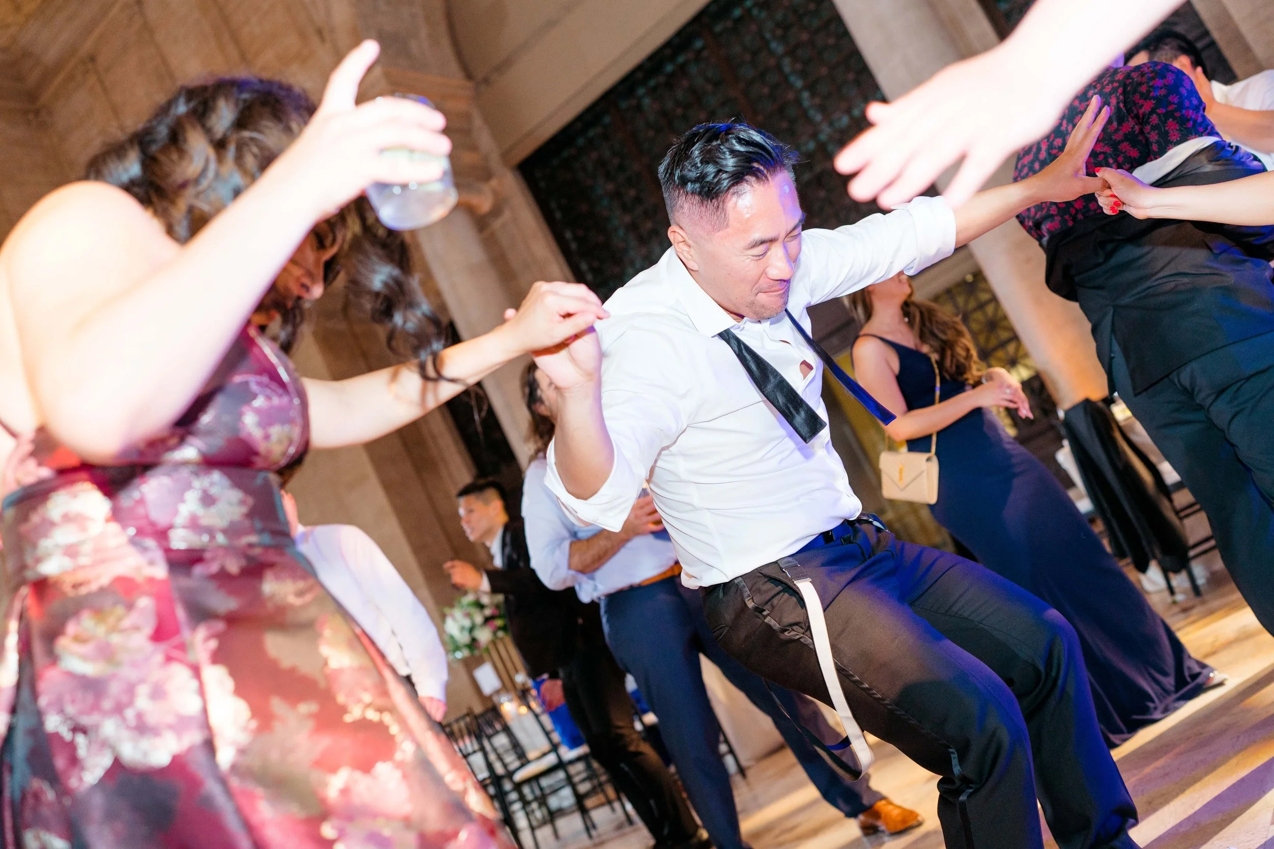 People dancing and celebrating at a party or wedding reception in an elegant venue with high ceilings and wooden walls.