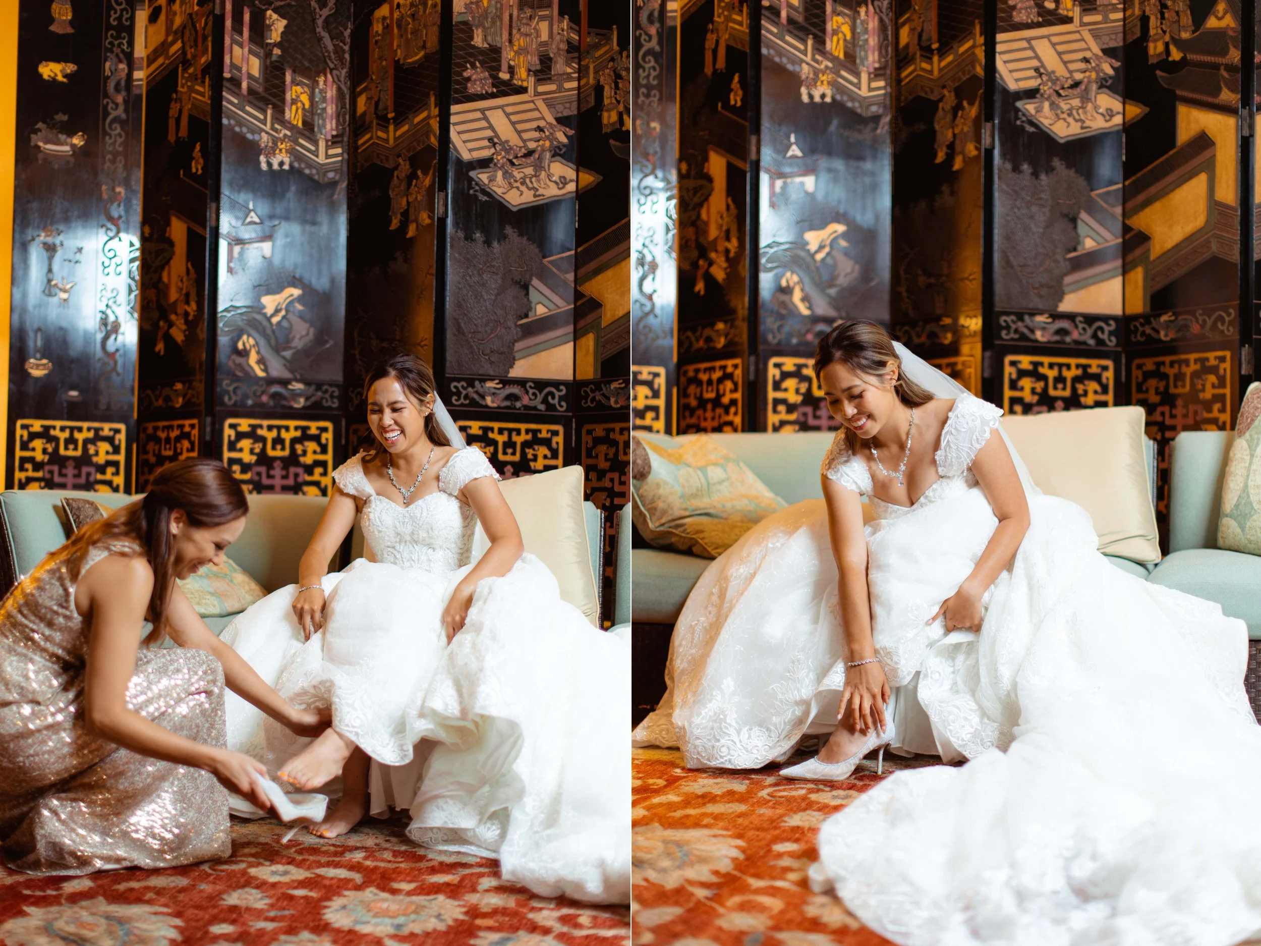 A bride in a white wedding dress is sitting on a sofa, smiling as another woman helps her put on shoes in a room with traditional Asian-themed decor and a decorative screen in the background.