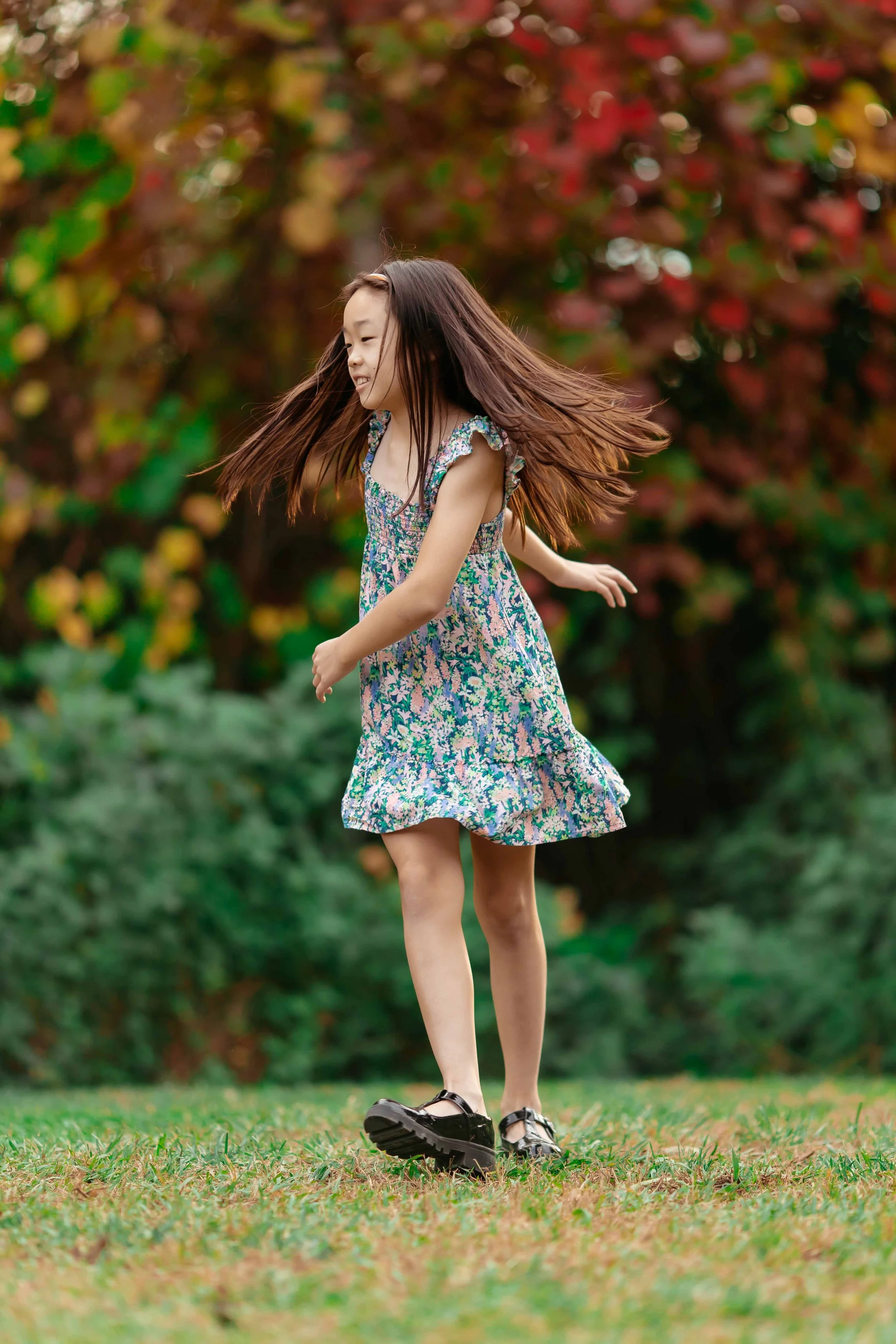 Young girl in a floral dress spinning and smiling in a park with colorful autumn trees.
