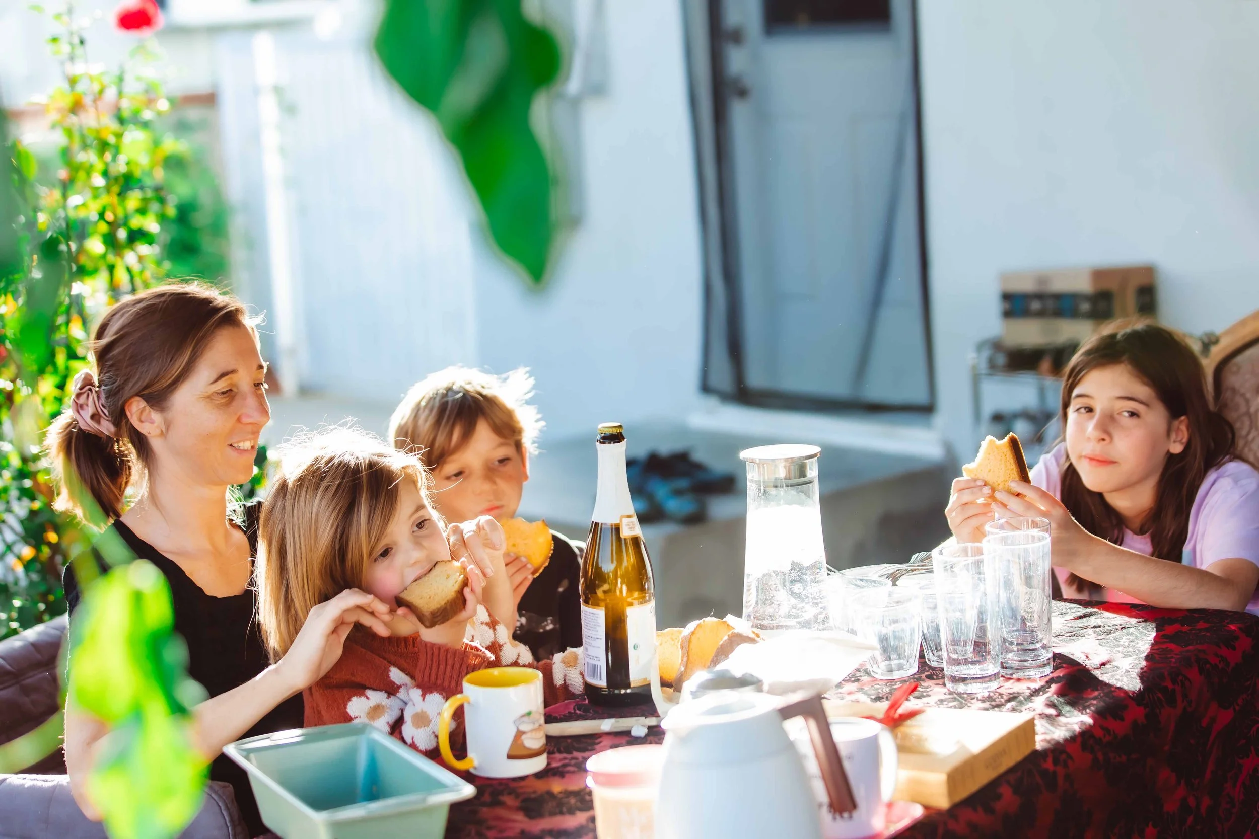 A family gathered around a table outdoors, eating sandwiches and drinking beverages during daylight hours.
