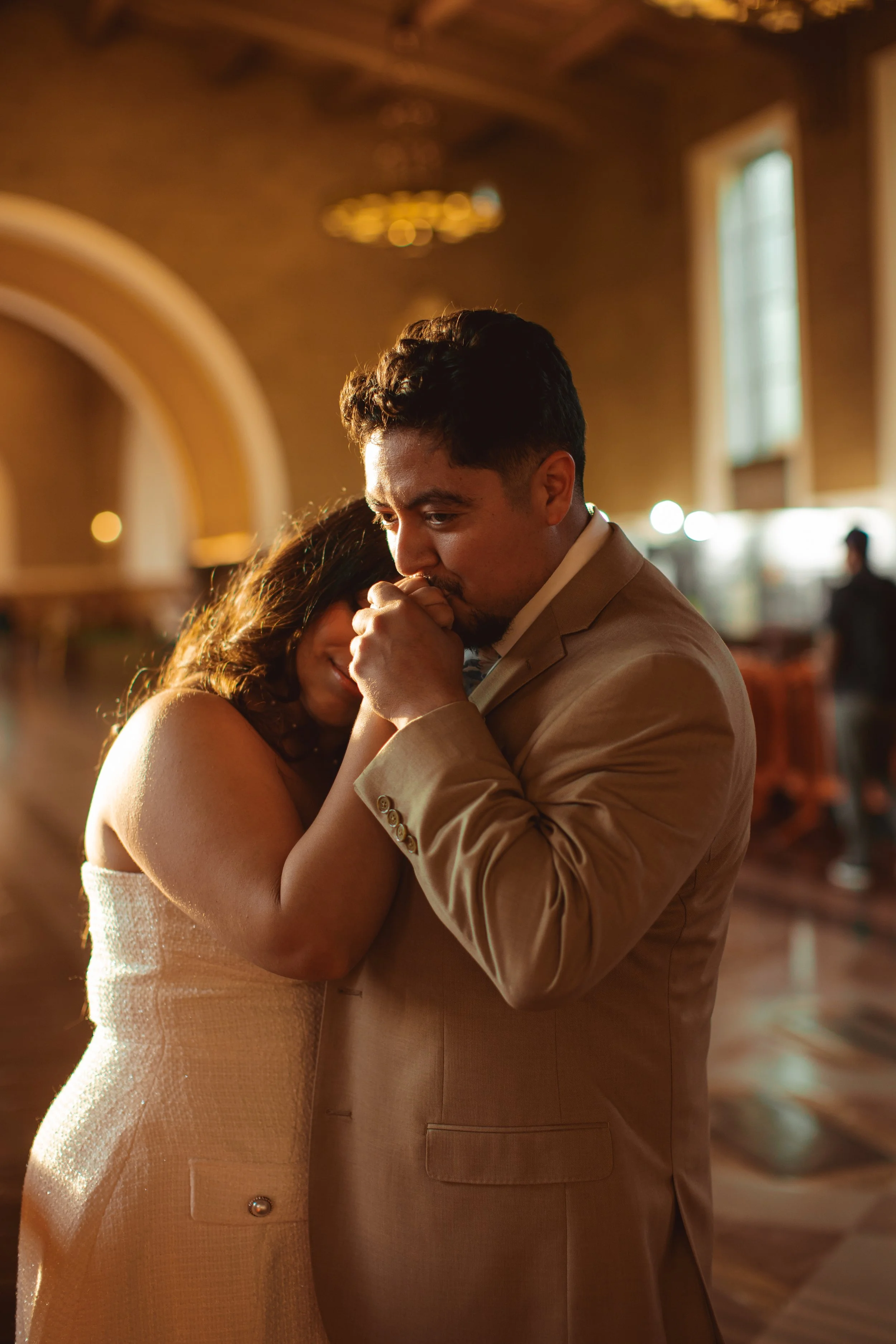 A man and a woman share an emotional moment indoors, with the man holding the woman's hand near his face.