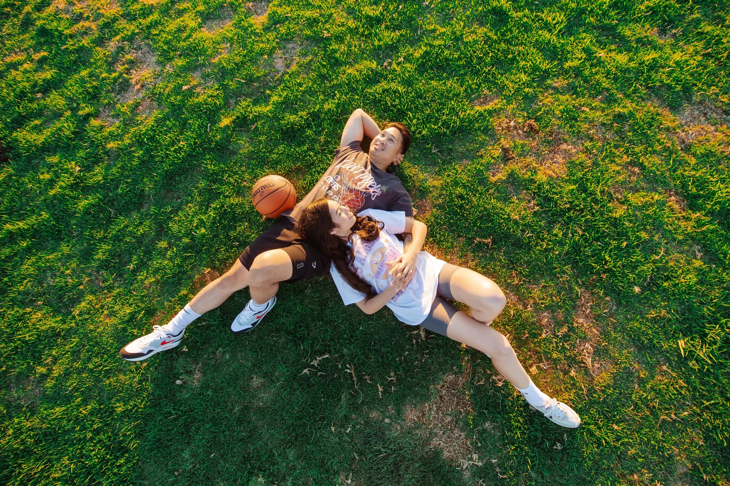 Two young people lying on grass after playing basketball, with a basketball nearby, during sunset.