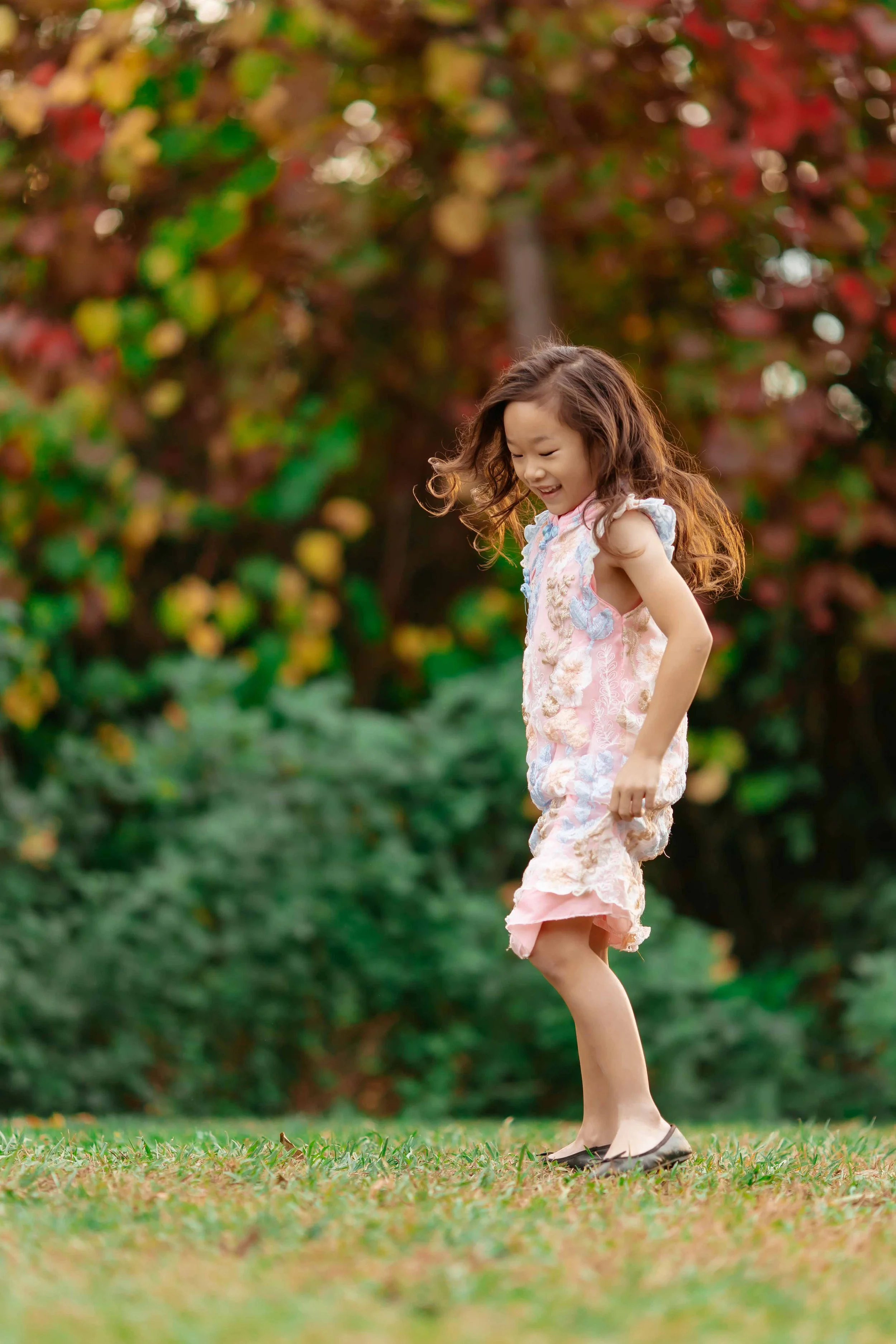 A young girl with curly hair playing on a grassy field with autumn-colored trees in the background.