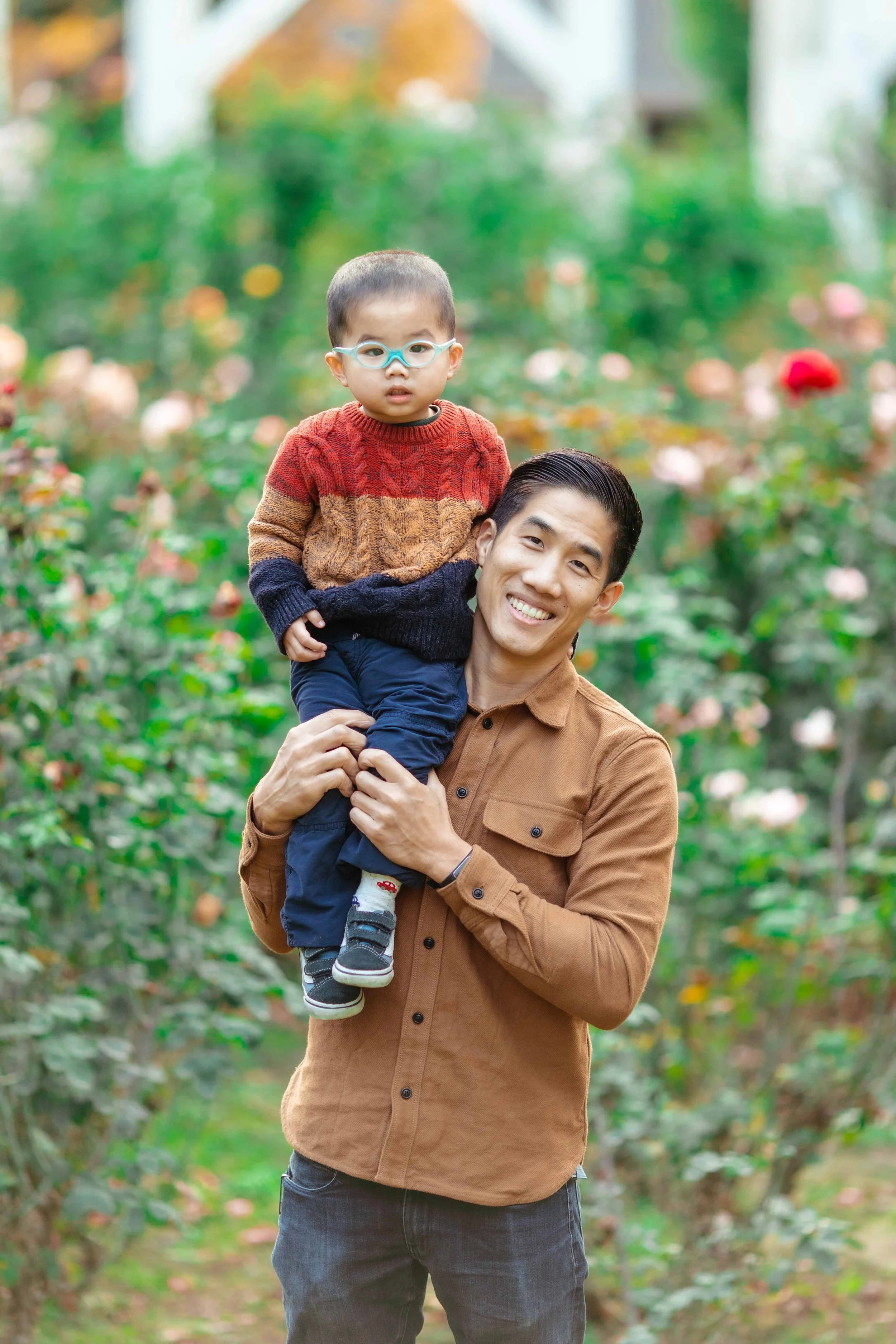 A man is holding a young boy on his shoulder in a garden with colorful flowers.