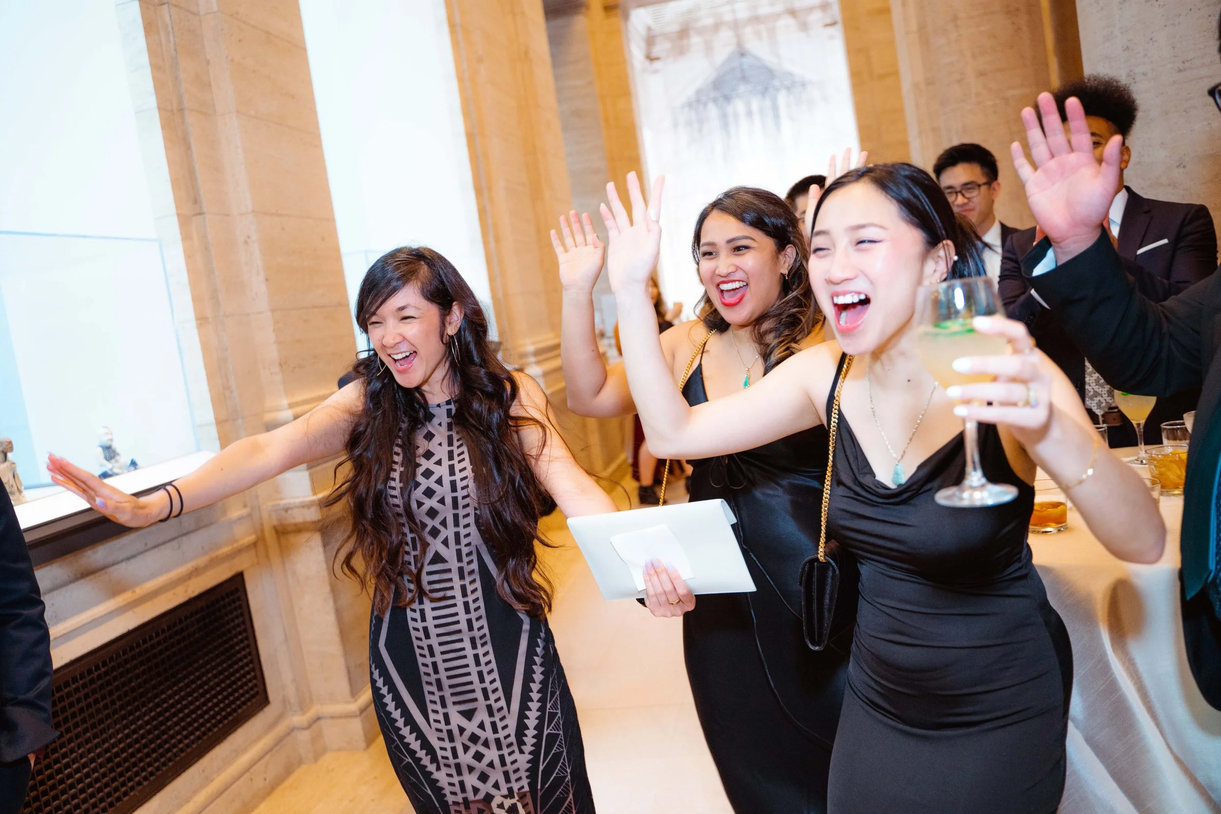 Group of women at a party happily dancing and raising hands, one woman holding a wine glass